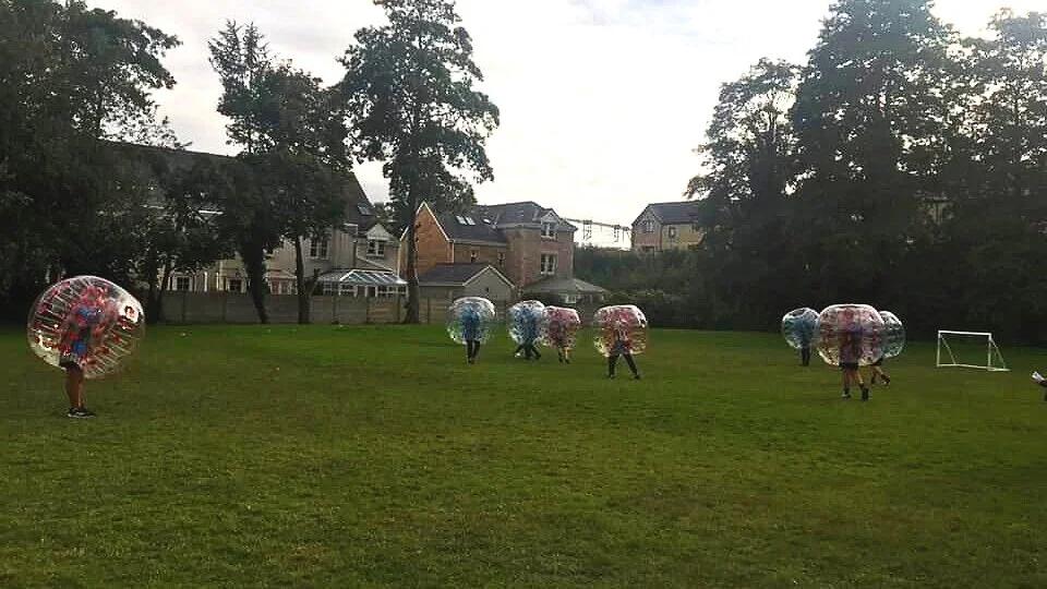 Young people playing bubble football inside zorb balls on a playing field