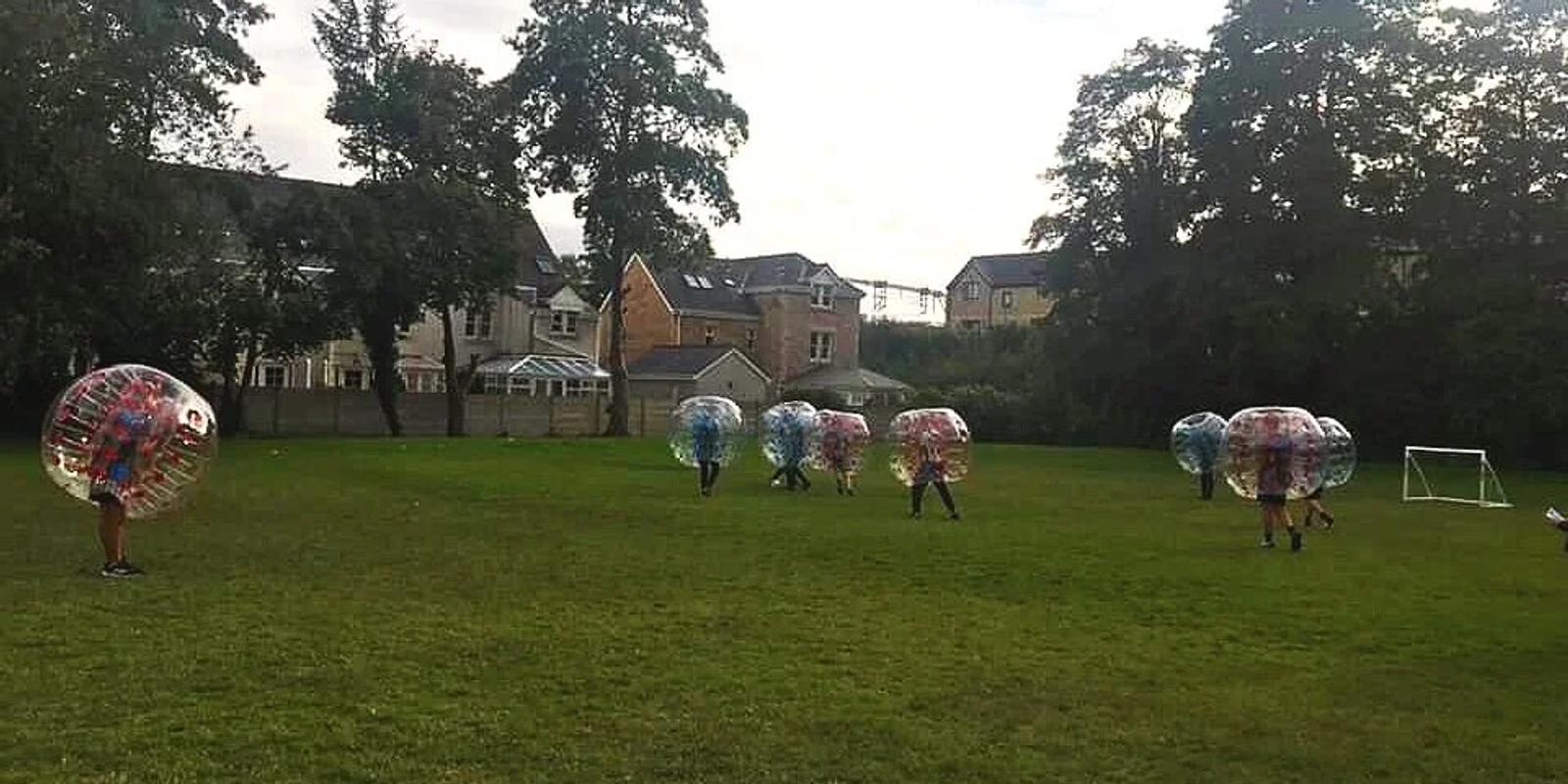 Young people playing bubble football inside zorb balls on a playing field