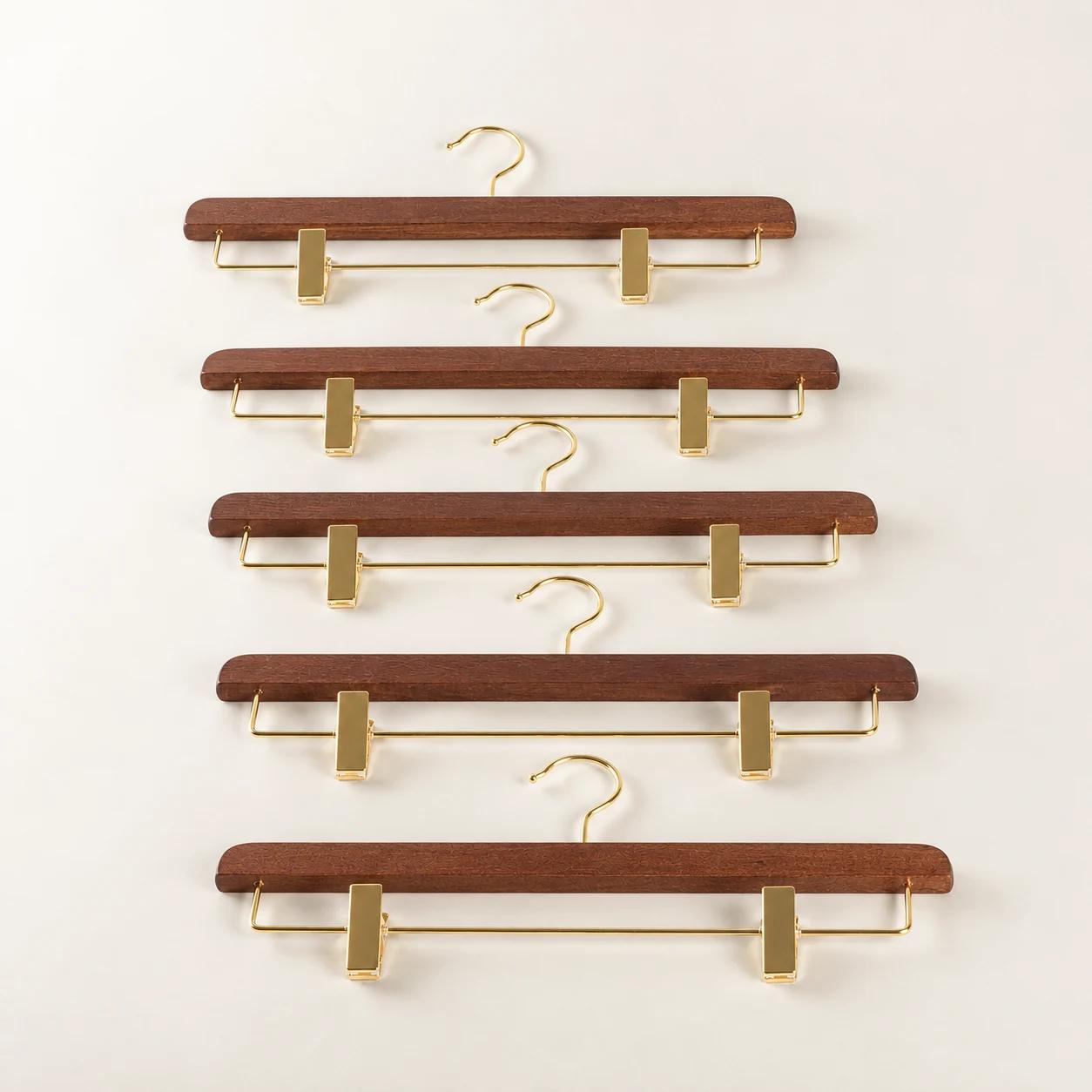 Five brown wooden clip hangers with gold-tone hooks and clips arranged on an ivory background