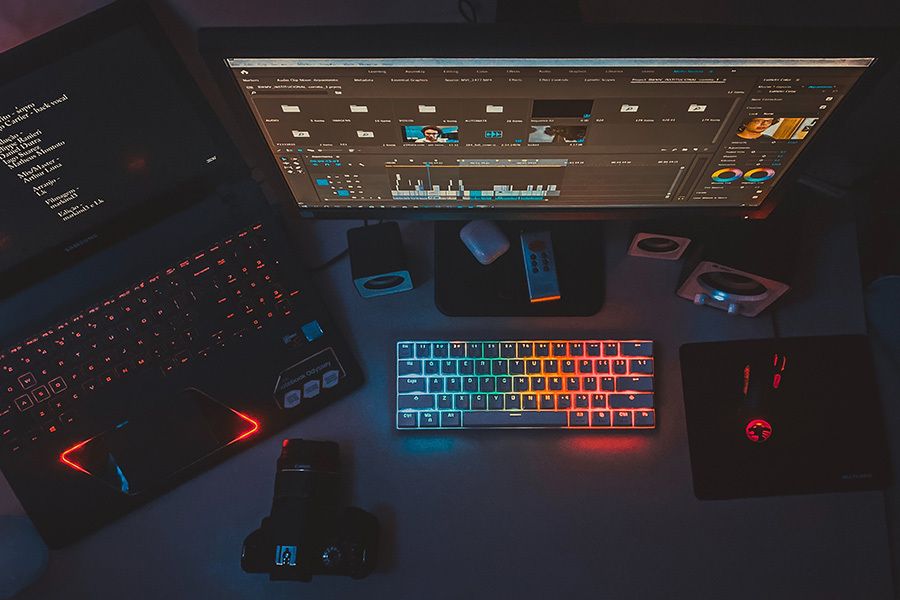Editing desk from above with a monitor running editing software, a backlit keyboard, laptop and camera