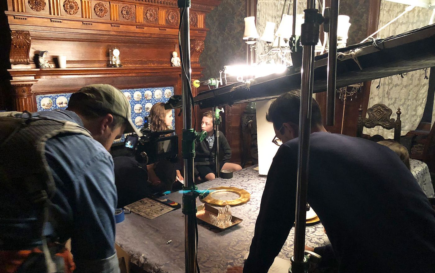 Crew filming actors Katherine Reis and Ryan Foust at a dining table on the set of Father Figurine