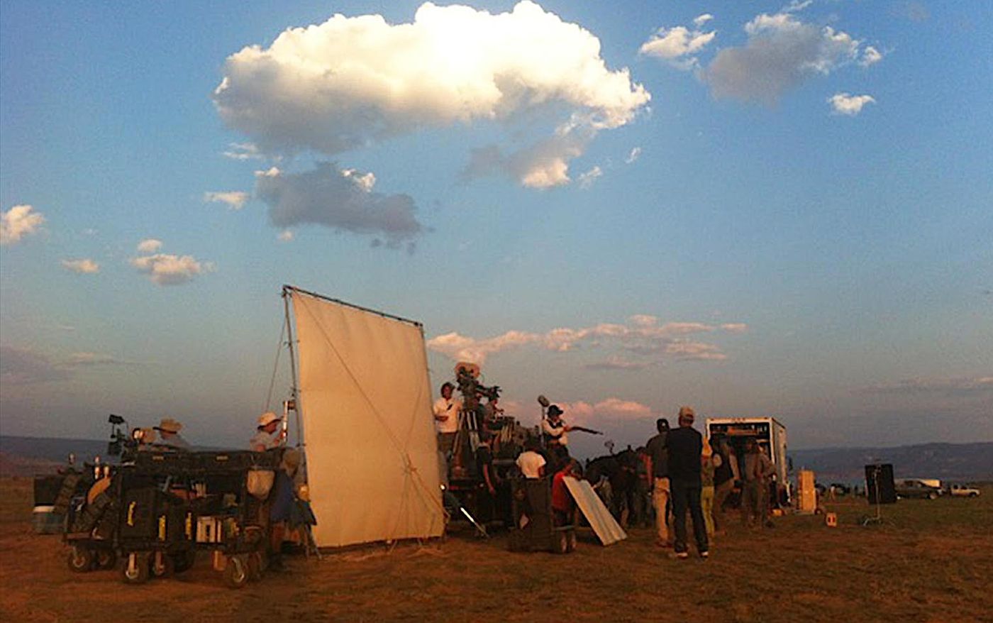 Film crew with a camera, reflector and equipment carts shooting outdoors at dusk on the set of Sweetwater (2013)