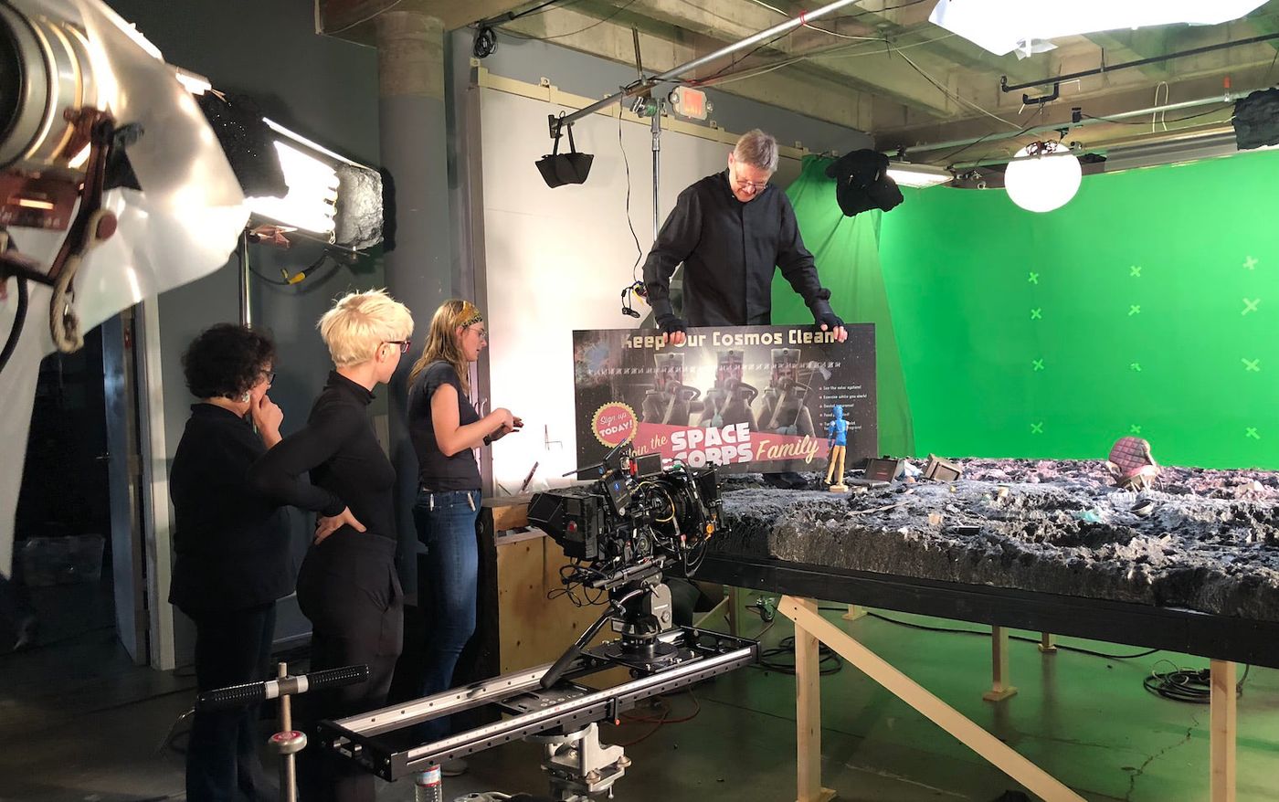 Marionettist Phillip Huber inspects the miniature set on a green screen stage as the crew looks on