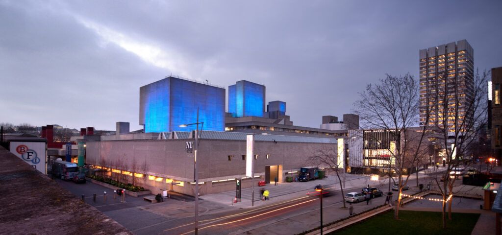 National Theatre building on London's South Bank at dusk, its fly towers lit blue