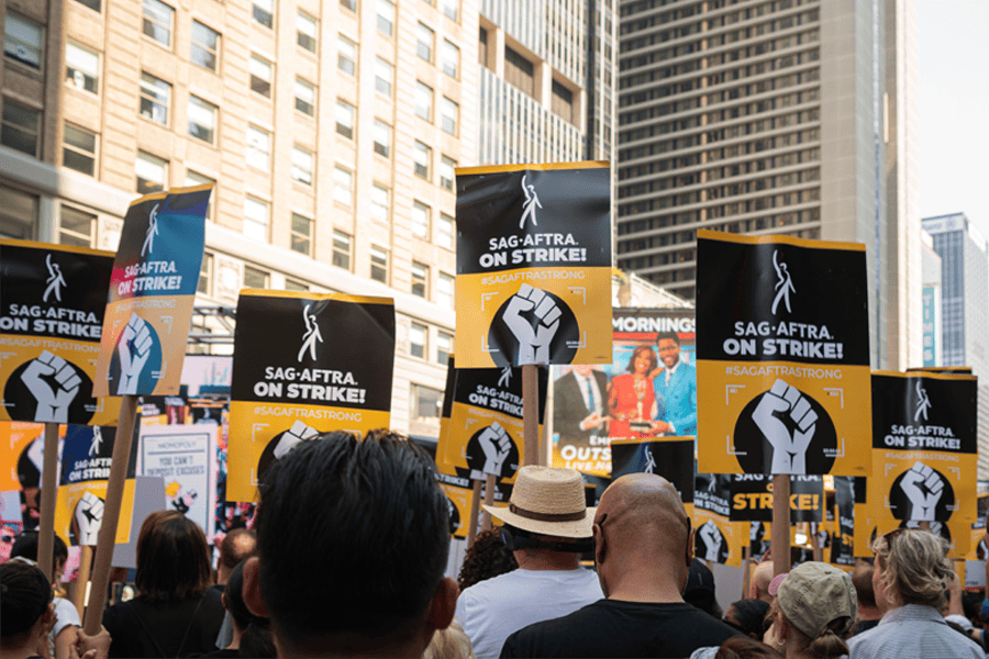 Crowd of protesters holding SAG-AFTRA On Strike! picket signs on a city street