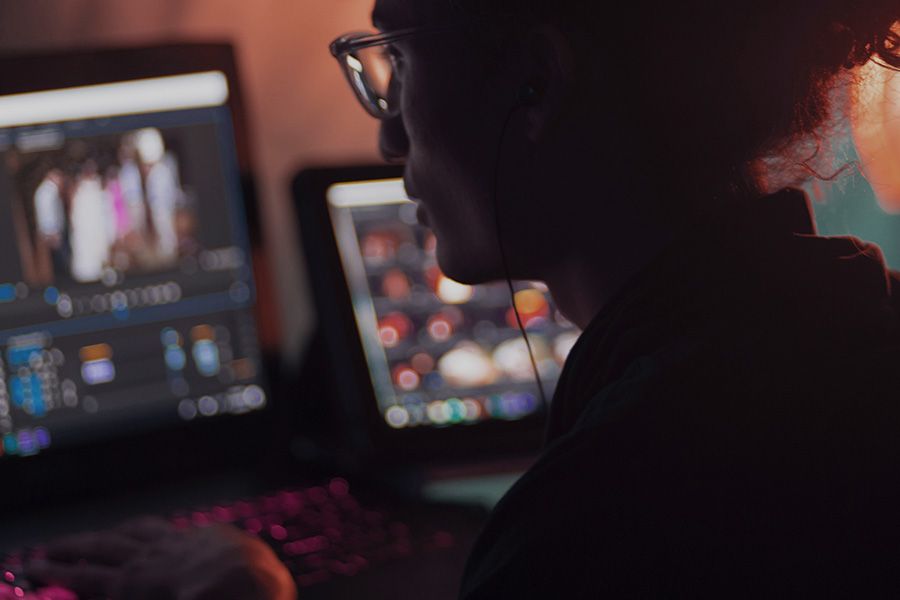 Editor in glasses working at dimly lit monitors in an edit suite