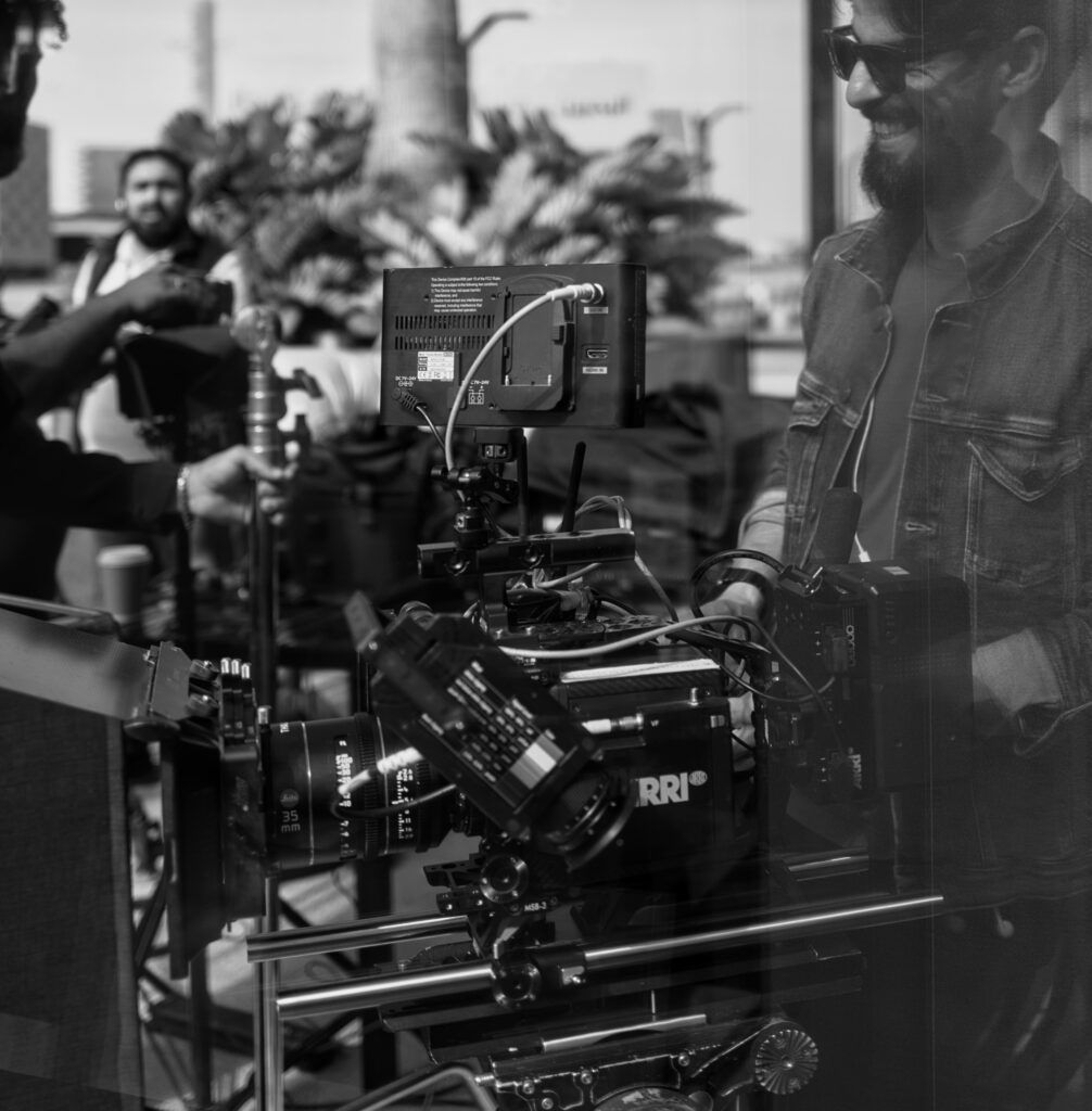 Black and white photo of an ARRI ALEXA cinema camera rig on set with crew in the background