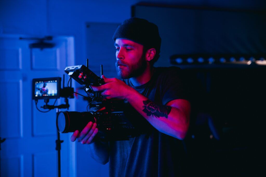 Camera operator adjusting a cinema camera with an attached monitor in blue and pink studio lighting