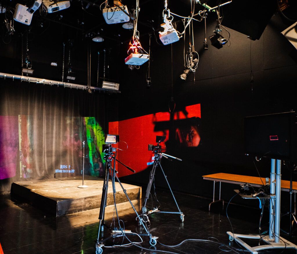 MassArt black box studio with cameras on tripods, a stage and overhead projectors