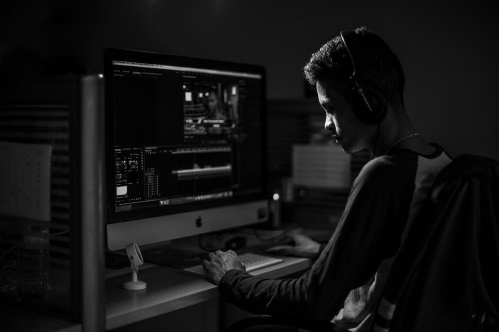 Editor wearing headphones working on a video timeline at an iMac, black and white