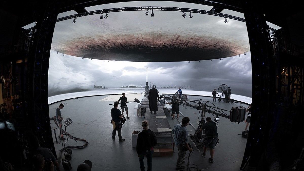 Virtual production stage with a curved LED volume showing a sky backdrop and film crew