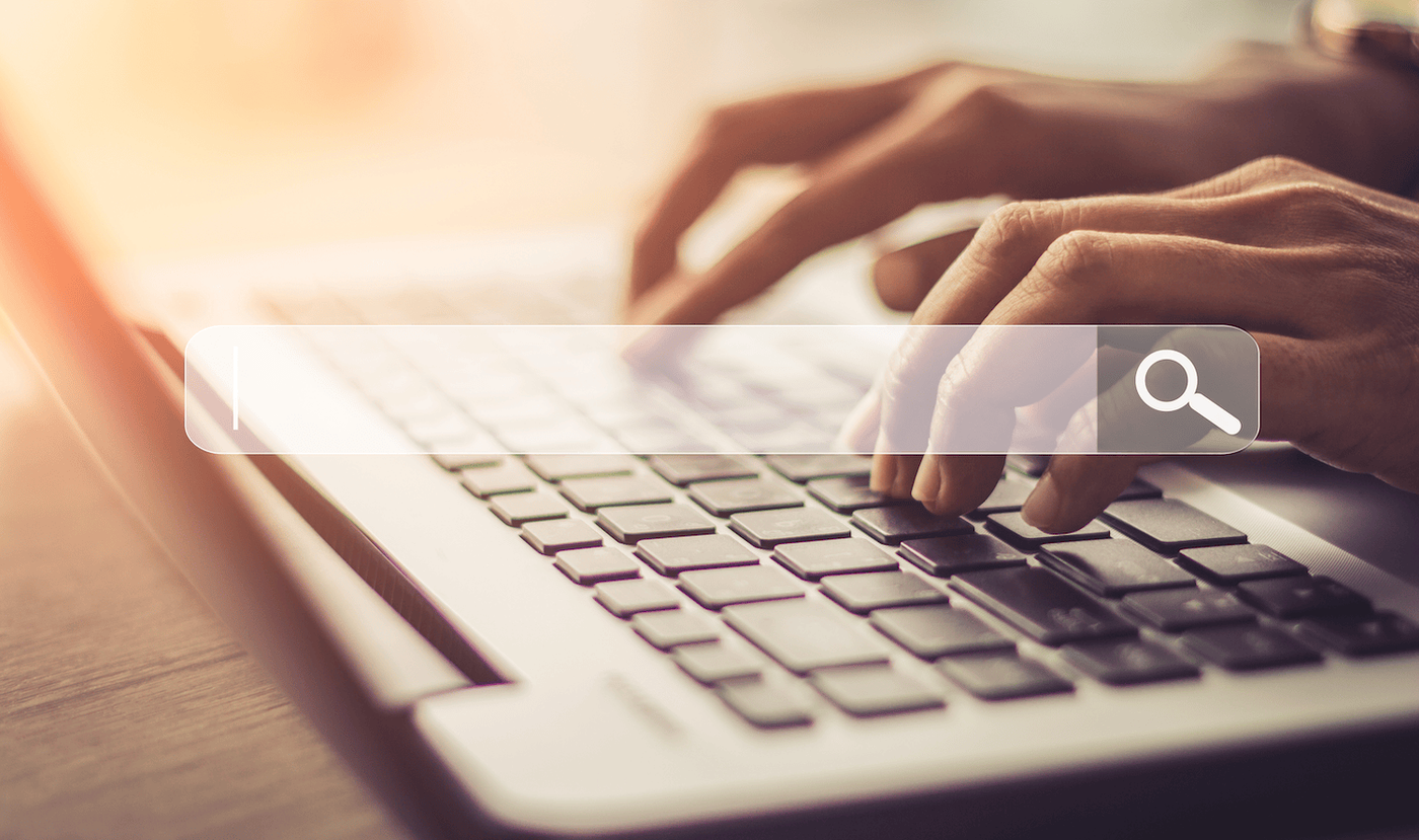 Hands typing on a laptop beneath a search bar graphic