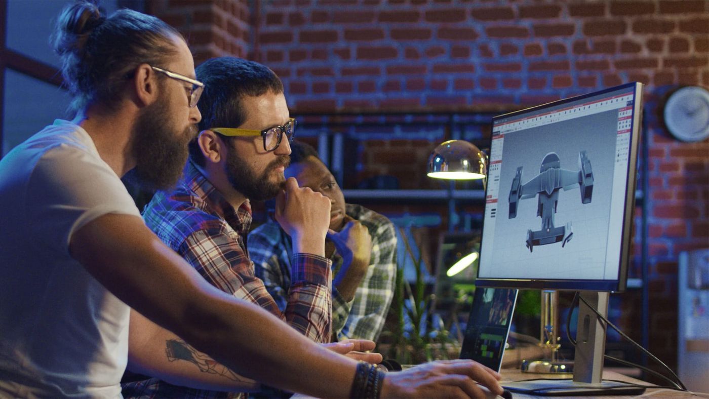 Game developers reviewing a 3D spaceship model on a monitor