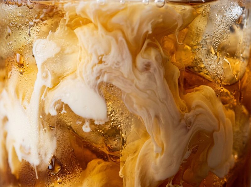 Macro shot of thick milk pouring into amber tea, marbled texture