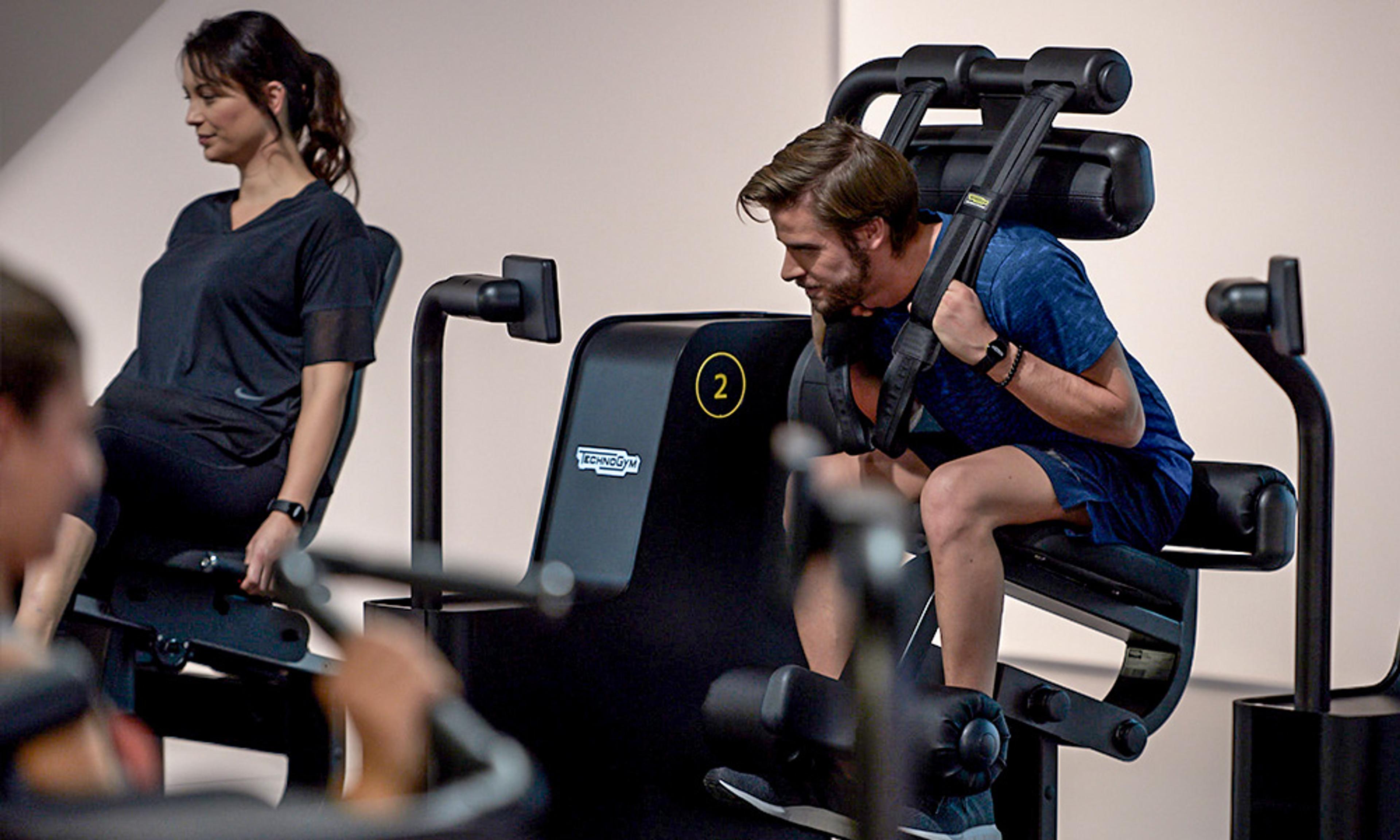 Zwei Personen trainieren an modernen Fitnessgeräten in einem Fitnessstudio