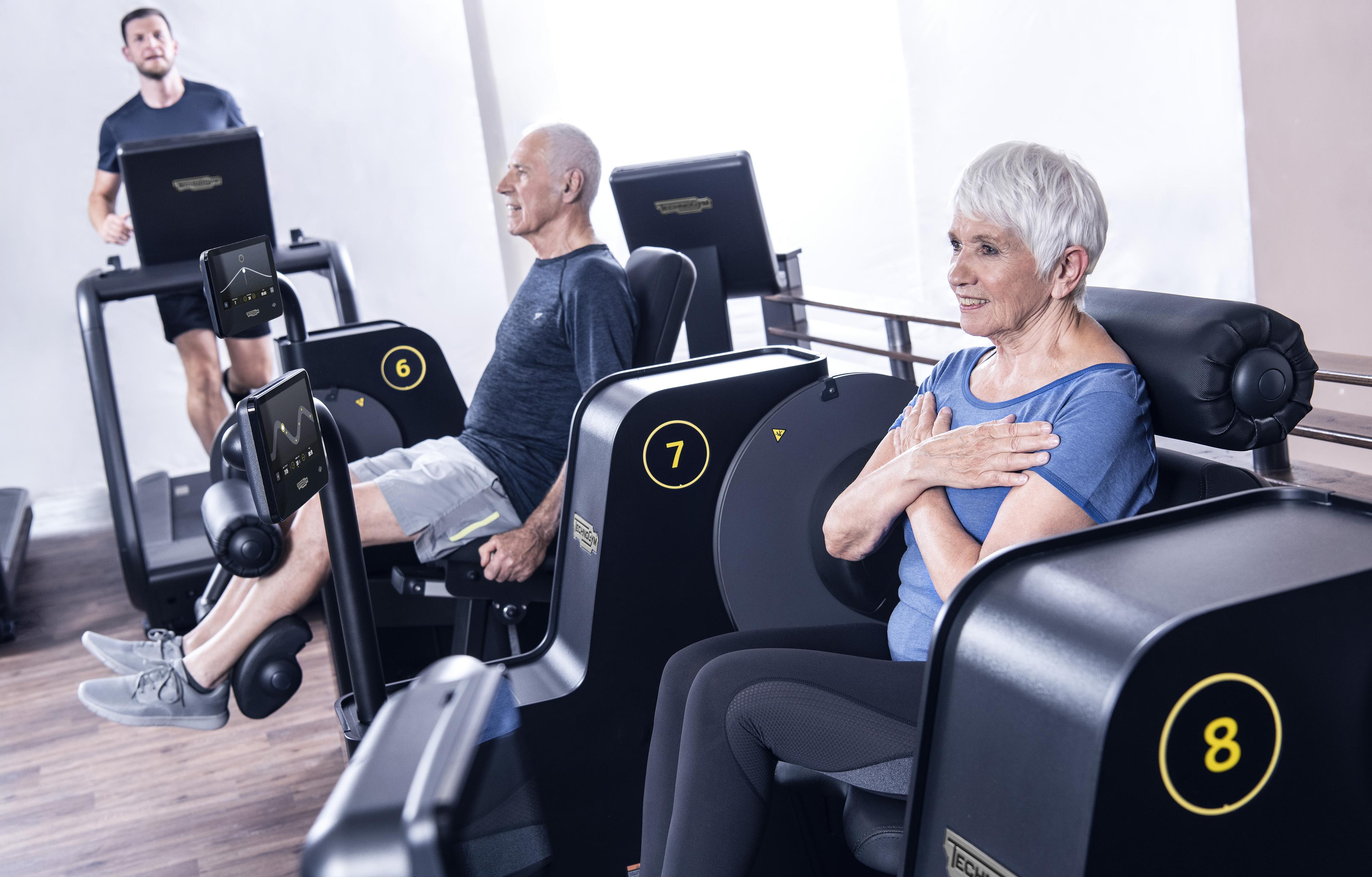 Ältere Menschen trainieren an modernen Fitnessgeräten in einem hellen Fitnessstudio