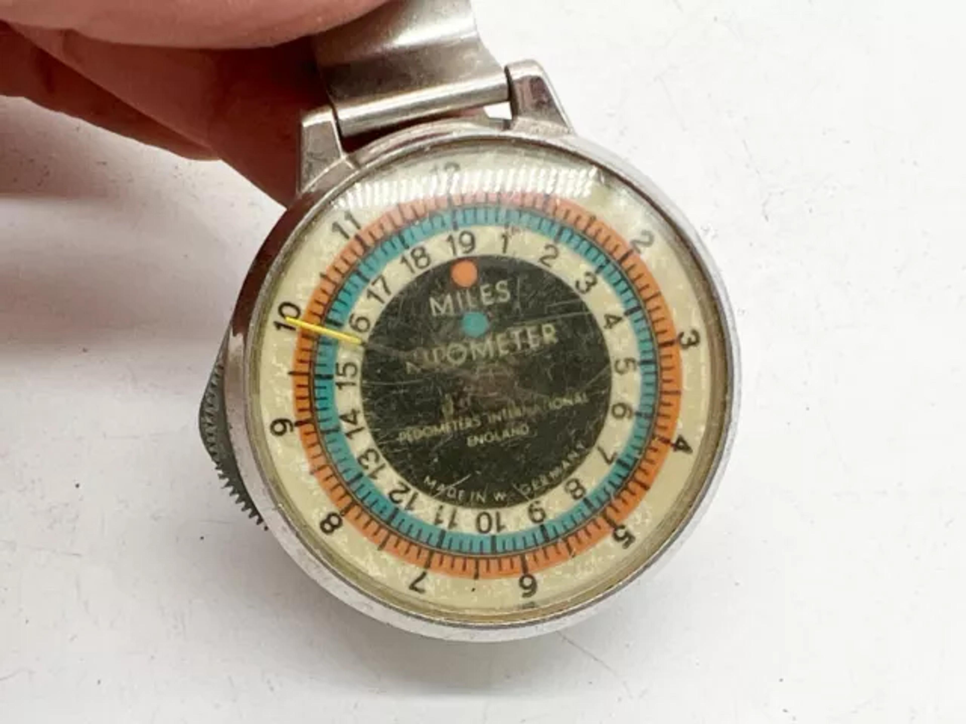 Ein handgehaltener Vintage-Schrittzähler aus Metall mit farbigen Skalen und Miles-Anzeige