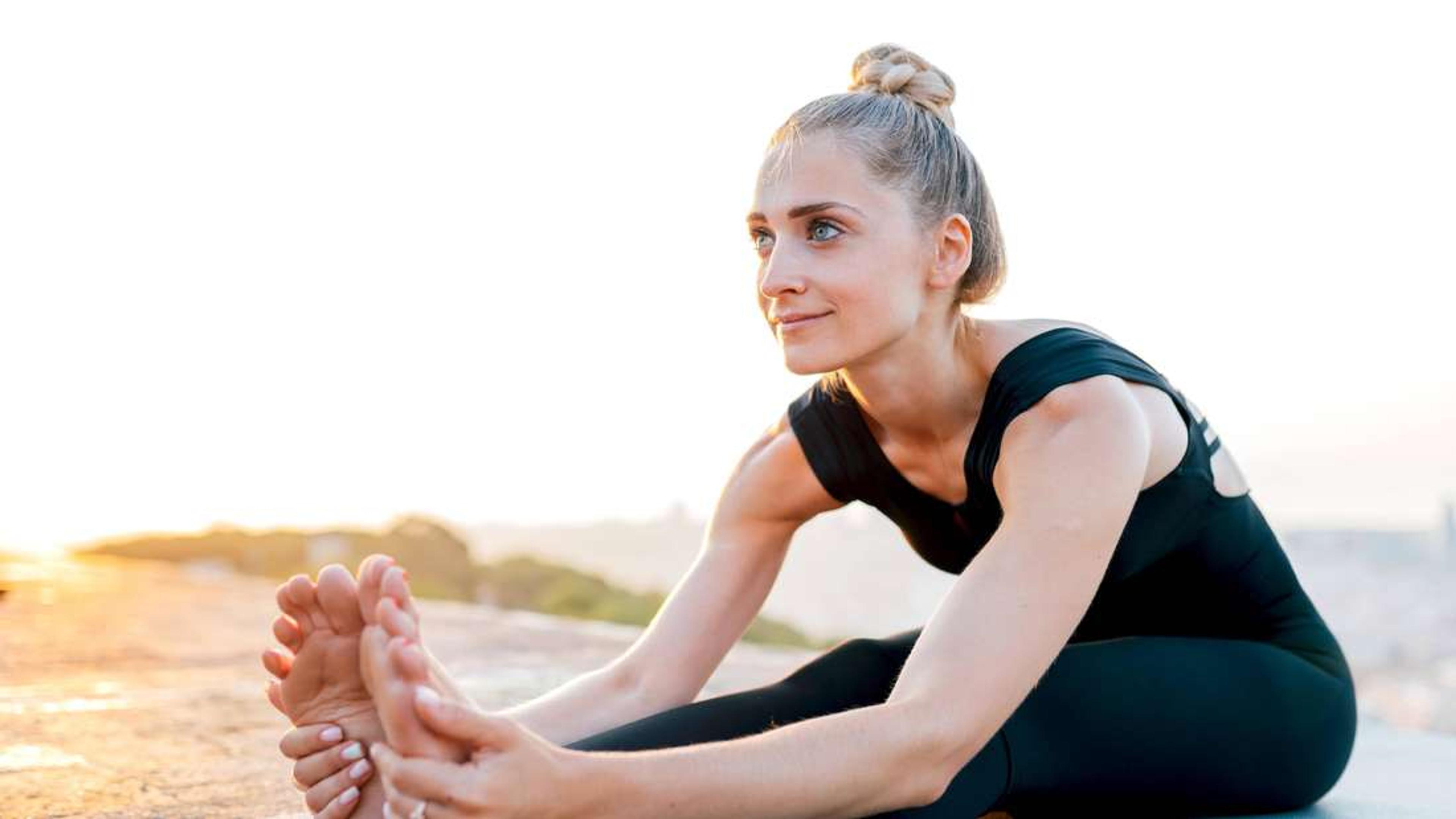 Eine Frau im schwarzen Sportoutfit streckt sich beim Yoga und berührt im Freien bei Sonnenaufgang ihre Zehen