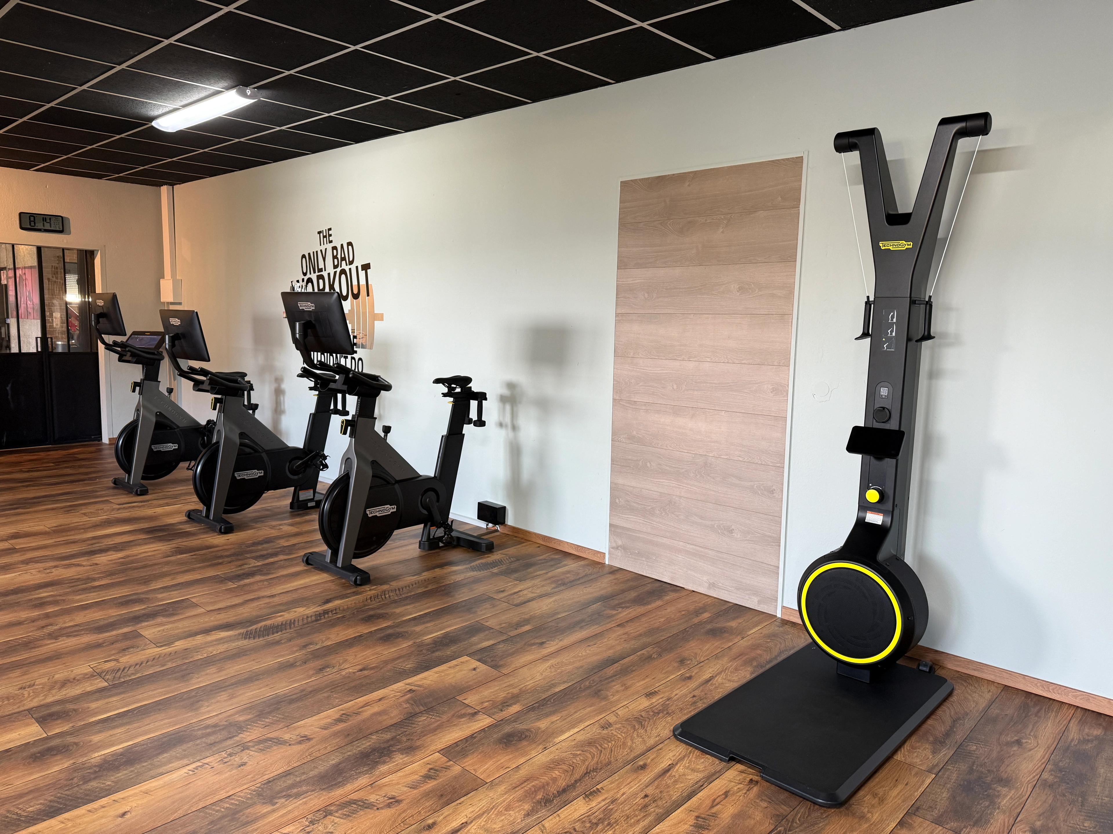 Ein Fitnessstudio mit drei modernen Spinningrädern und einem speziellen Trainingsgerät auf einem Holzboden