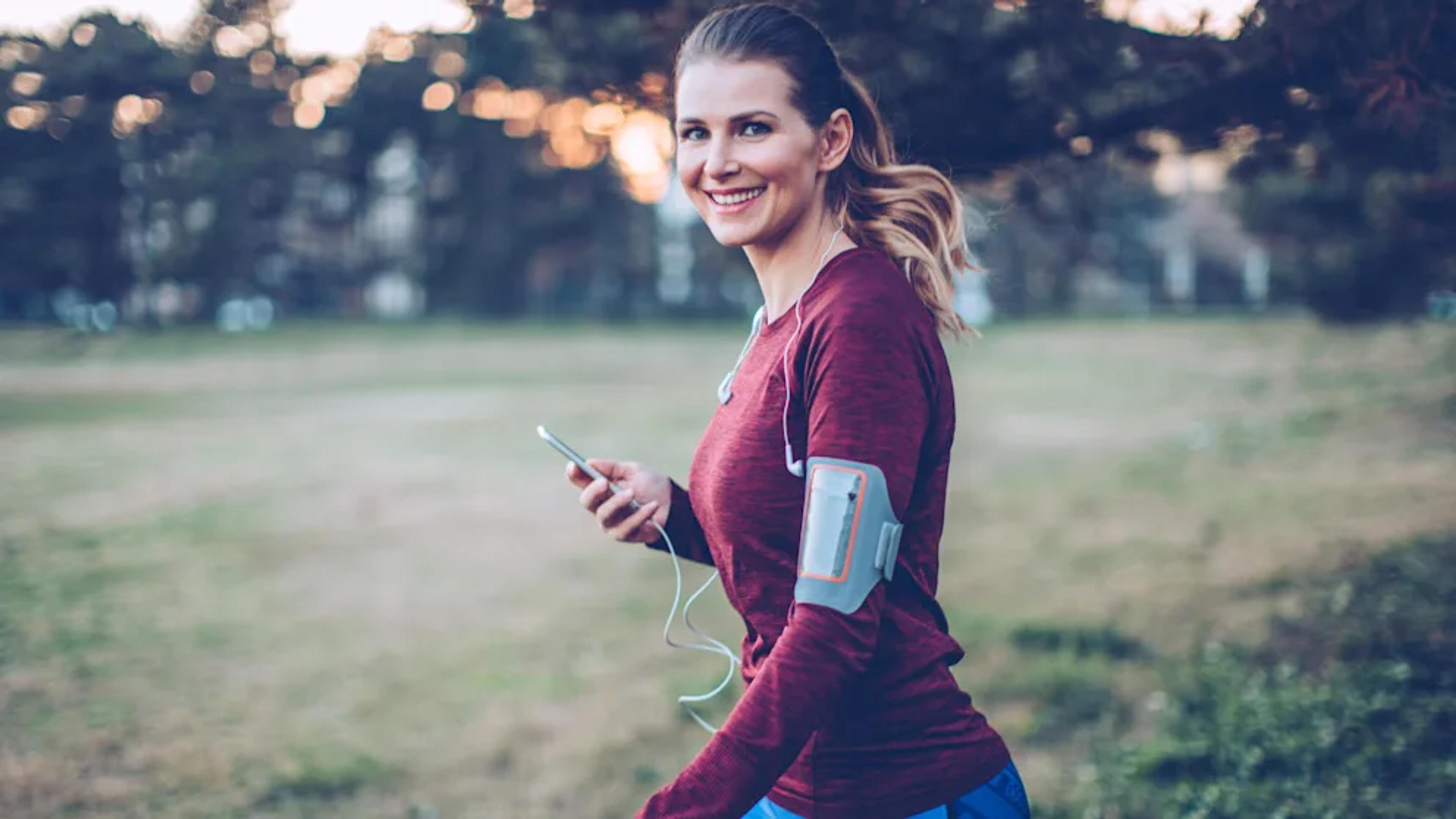 Eine junge Frau in Sportkleidung joggt im Park mit Smartphone und Kopfhörern