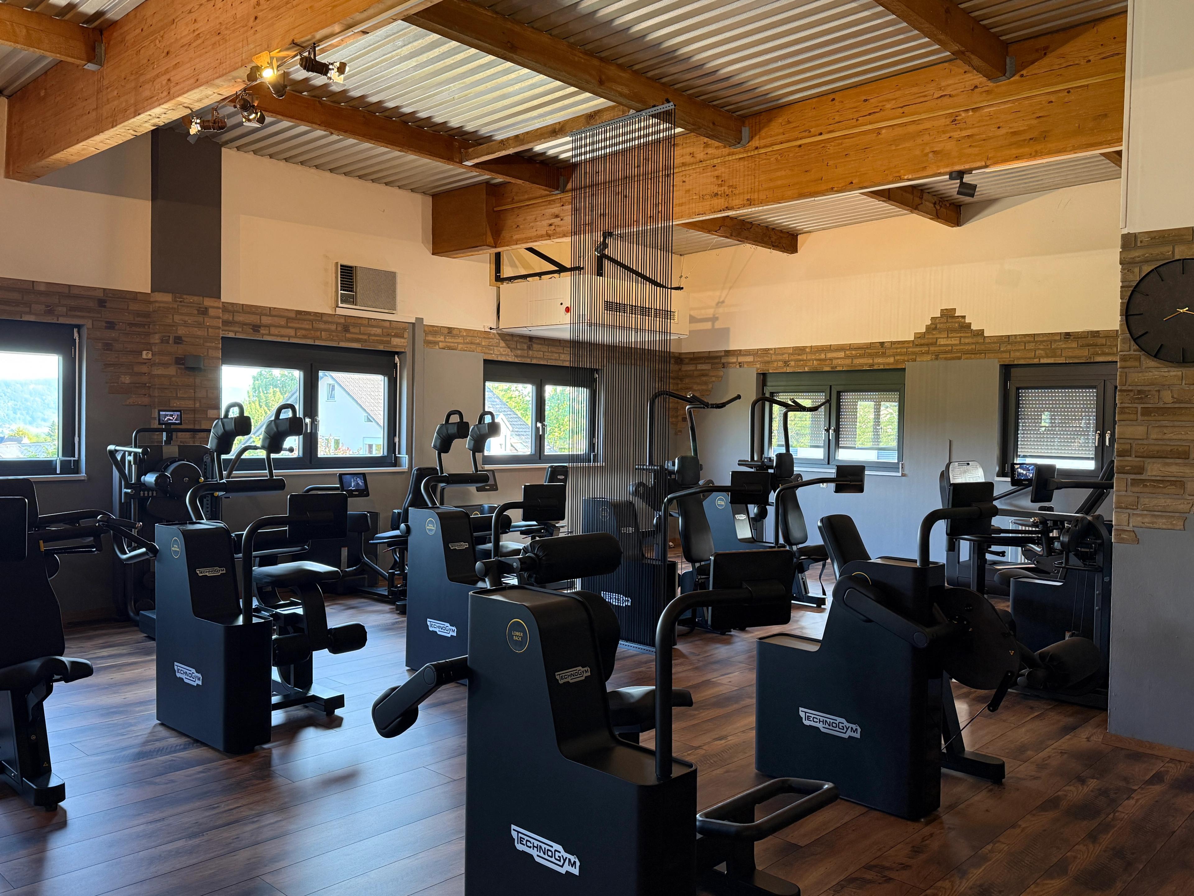 Ein geräumiger Fitnessraum mit zahlreichen Cardio-Geräten und Holzbalkendecke
