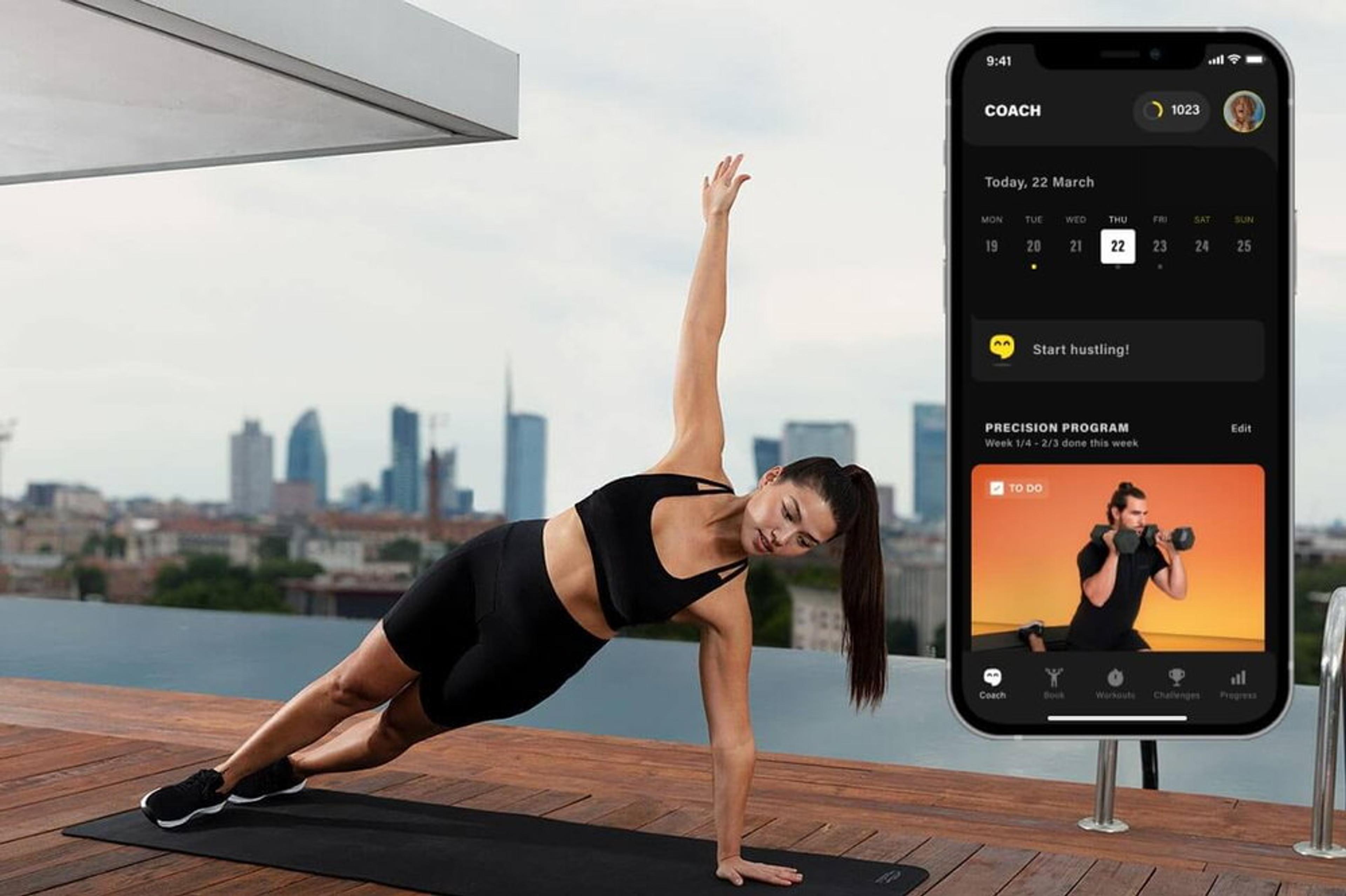 Eine Frau macht Yoga auf einer Dachterrasse mit einer Fitness-App auf einem Smartphone im Vordergrund.