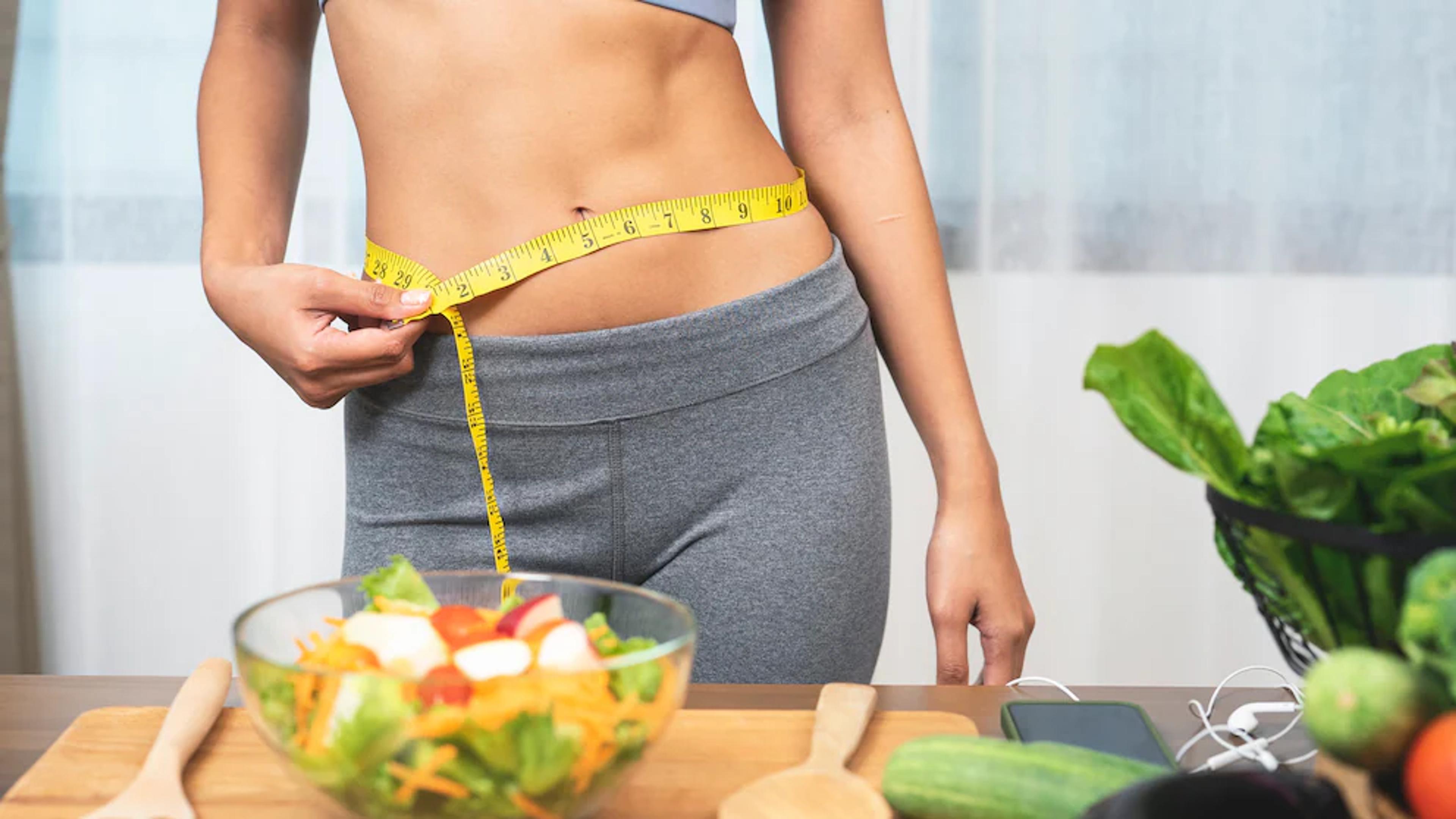 Frau misst ihre Taille mit einem Maßband neben einem frischen Salat