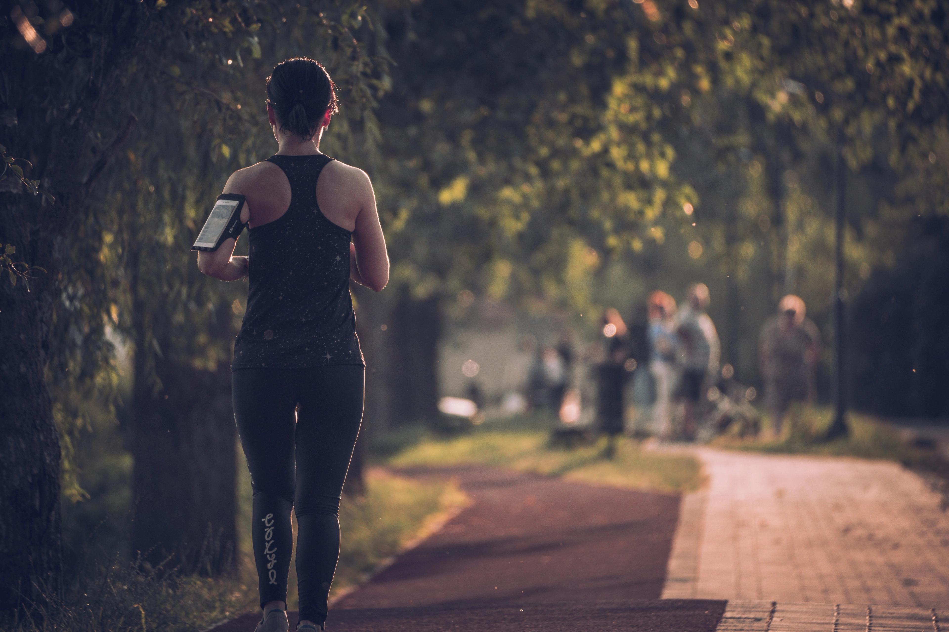 Eine Joggerin in Sportkleidung dehnt sich auf einem Weg im herbstlichen Park