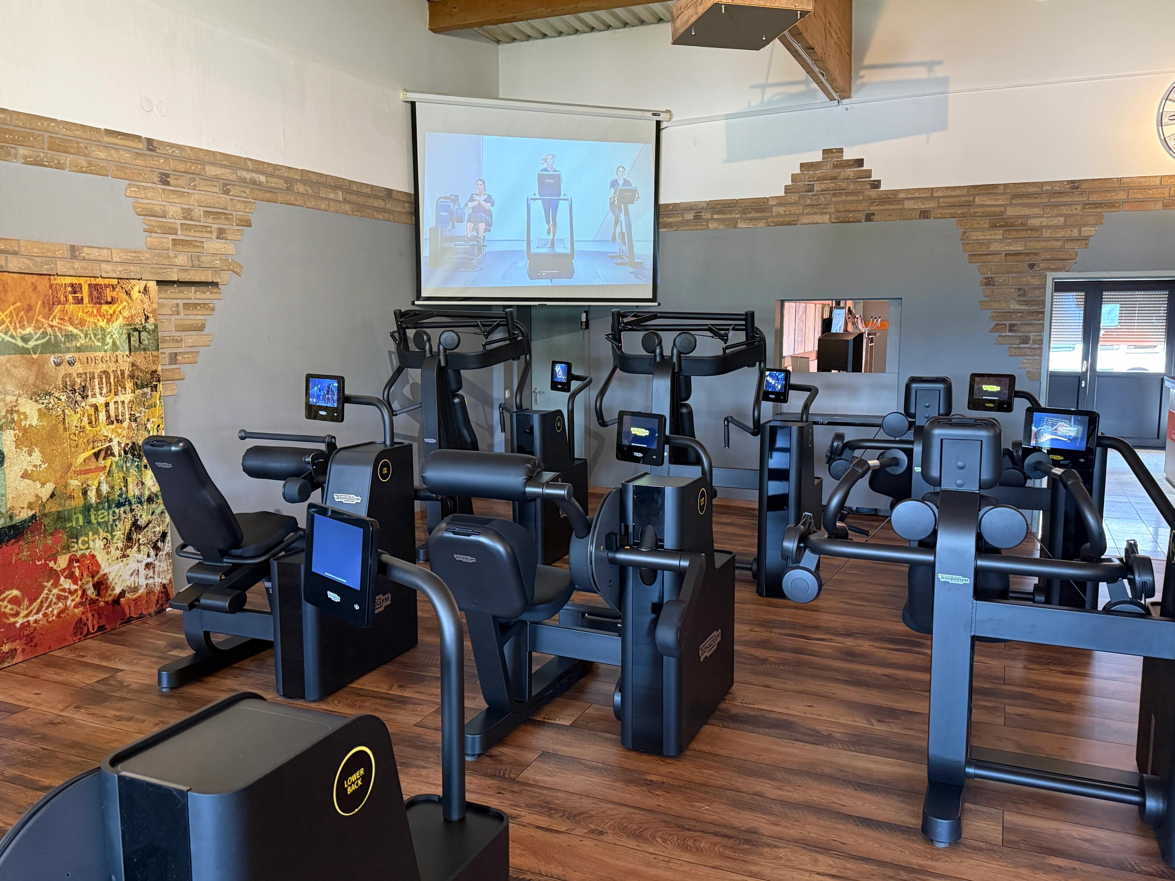 Ein moderner Fitnessraum ausgestattet mit digitalen Trainingsgeräten und einem Bildschirm für Trainingsanleitungen