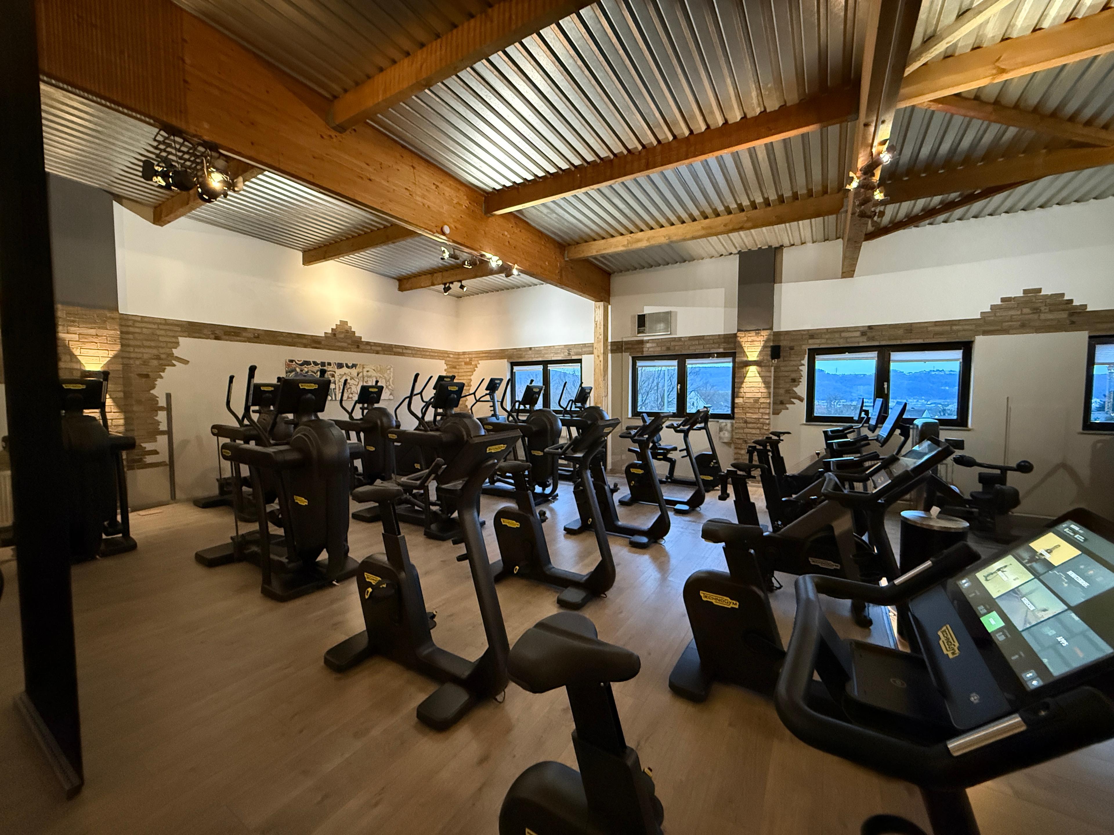 Ein modernes Fitnessstudio mit verschiedenen Cardio-Geräten, Holzdecke und großen Fenstern