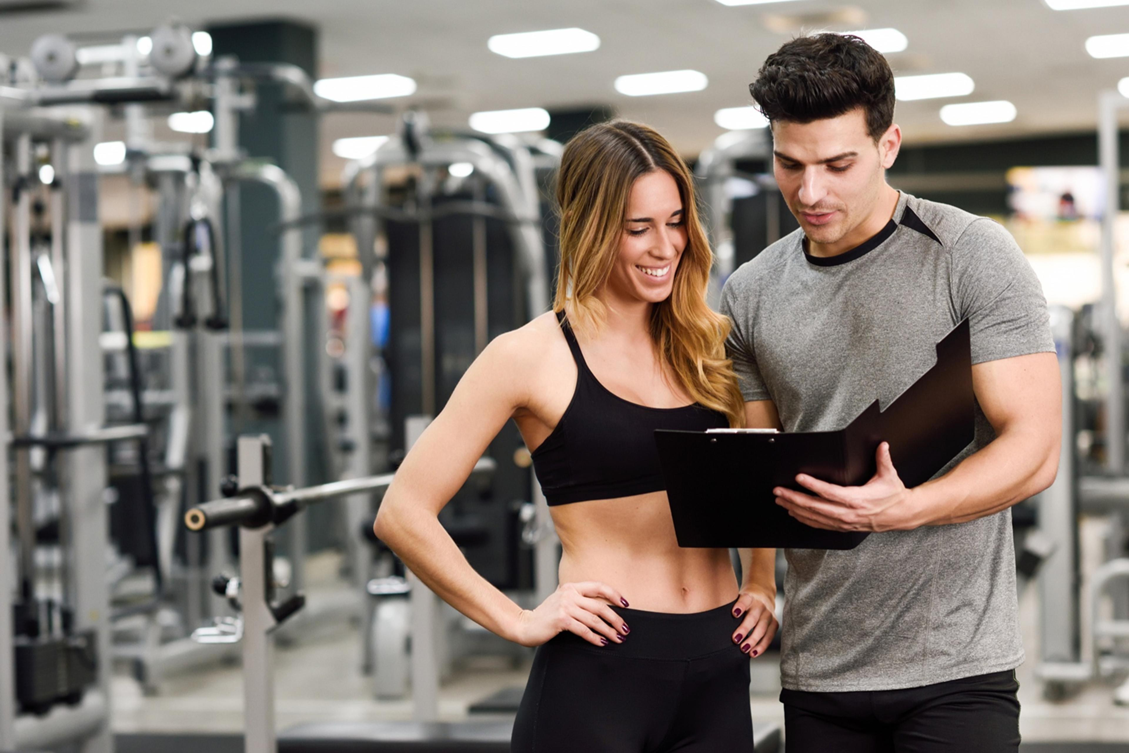 Ein Fitness-Trainer und eine Frau in Sportkleidung besprechen einen Trainingsplan im Fitnessstudio