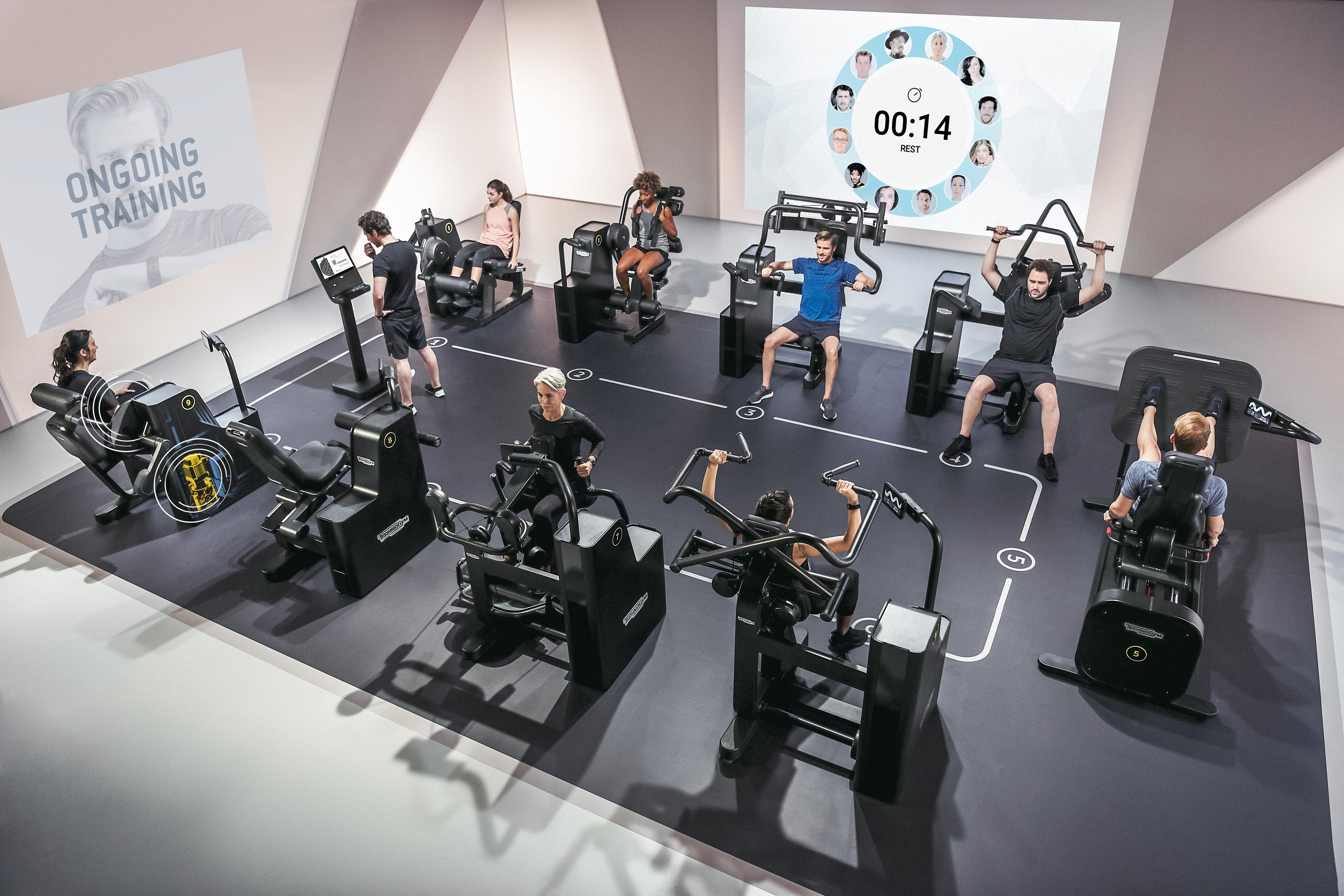 Mehrere Personen trainieren an modernen Fitnessgeräten in einem Studio mit digitaler Trainingsanzeige