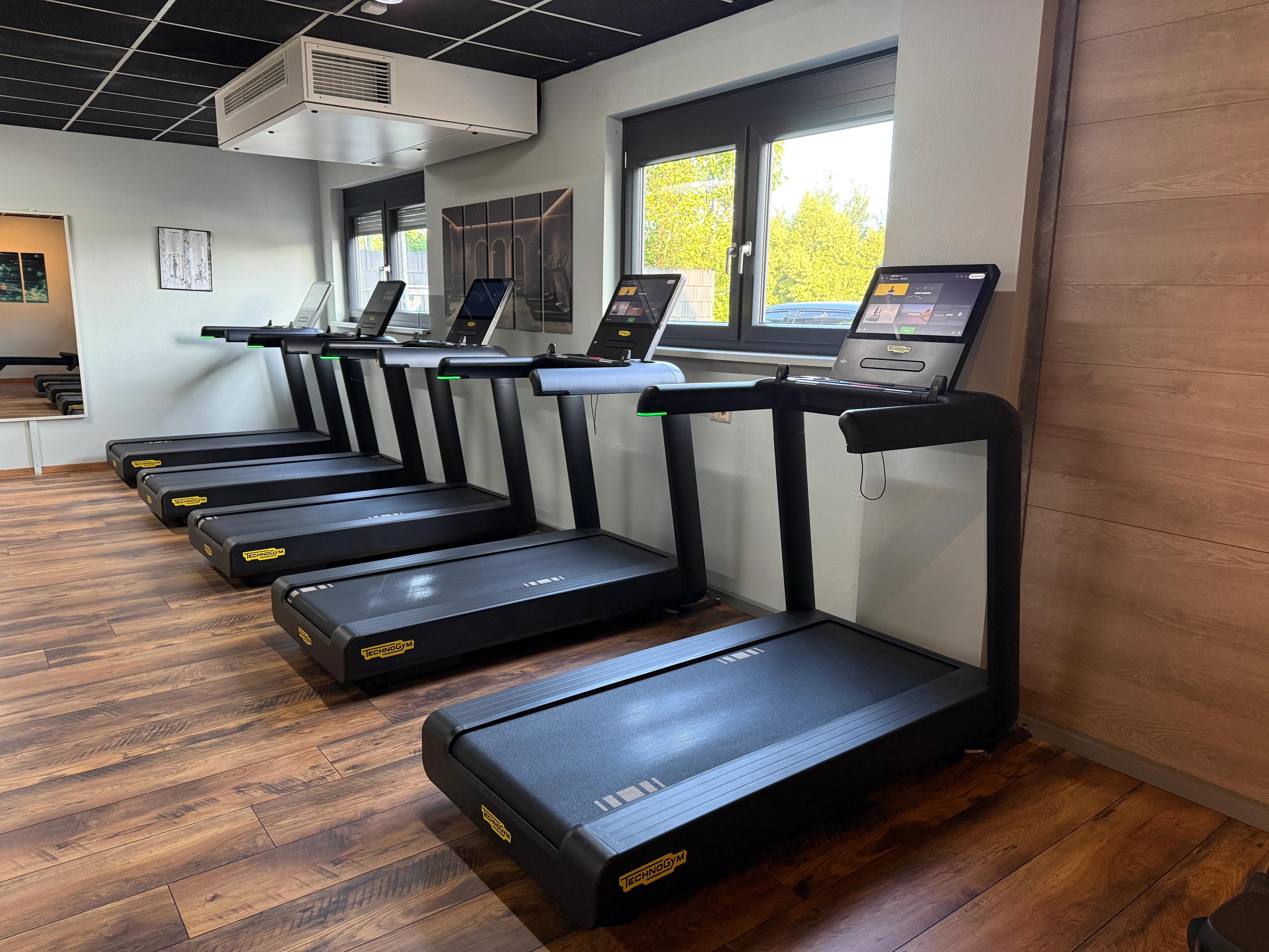 Ein moderner Fitnessraum mit verschiedenen Cardio-Geräten und Holzbalkendecke