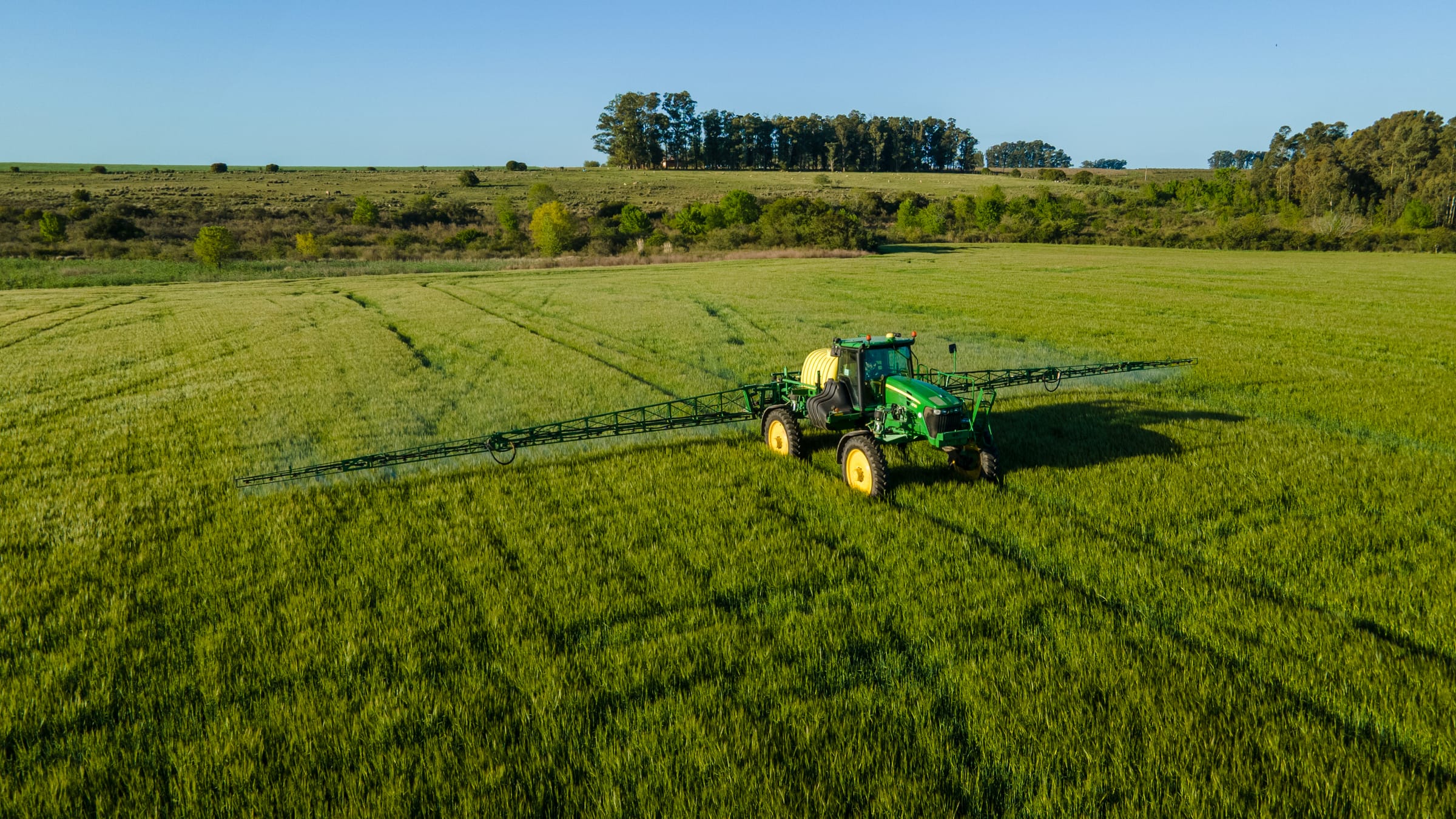 Pulverizadora con los botalones abiertos en un cultivo verde, vista aérea