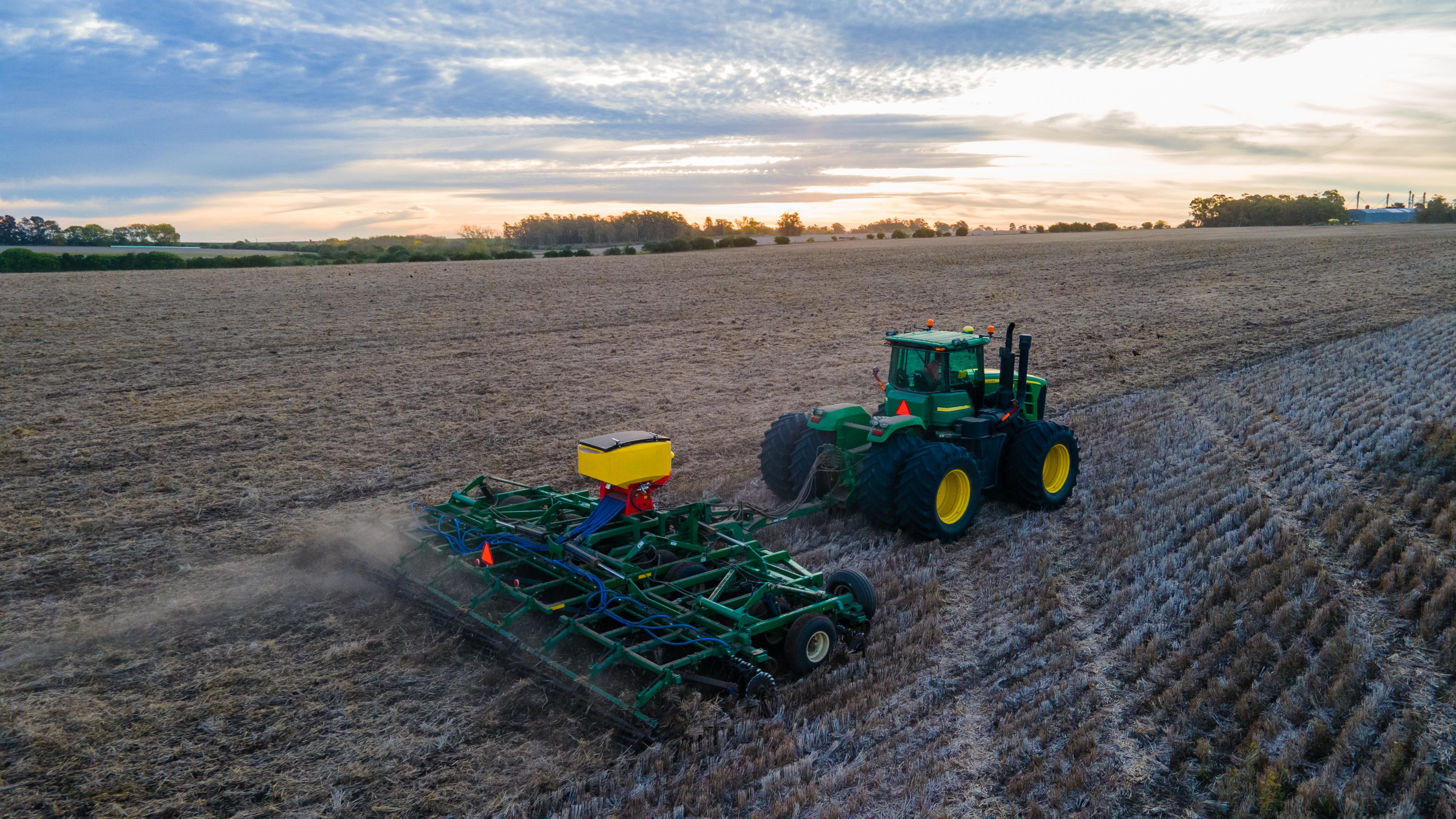 Tractor con equipo de siembra en el rastrojo al atardecer, vista aérea