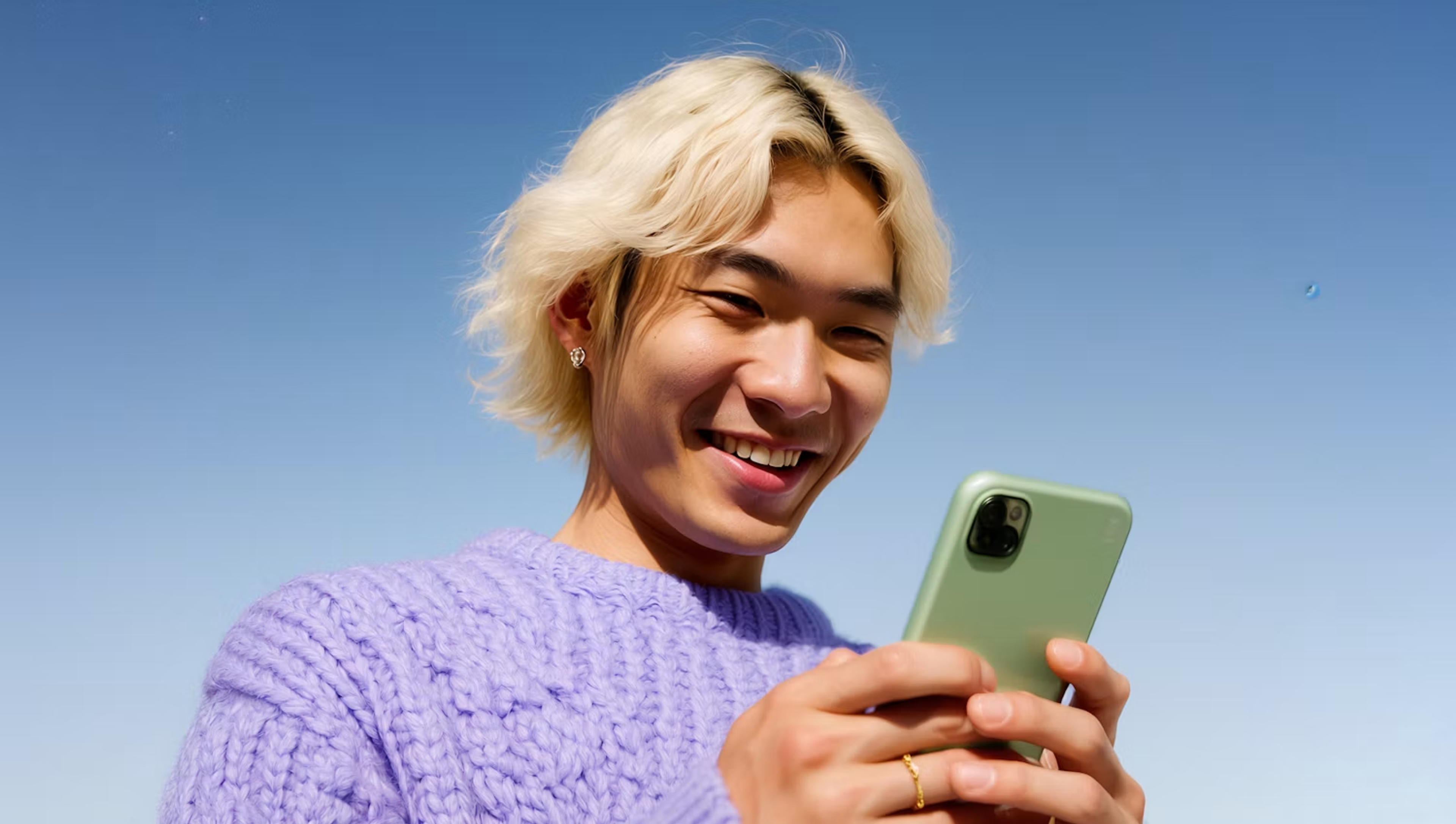 Smiling person in a lilac sweater looking at a phone