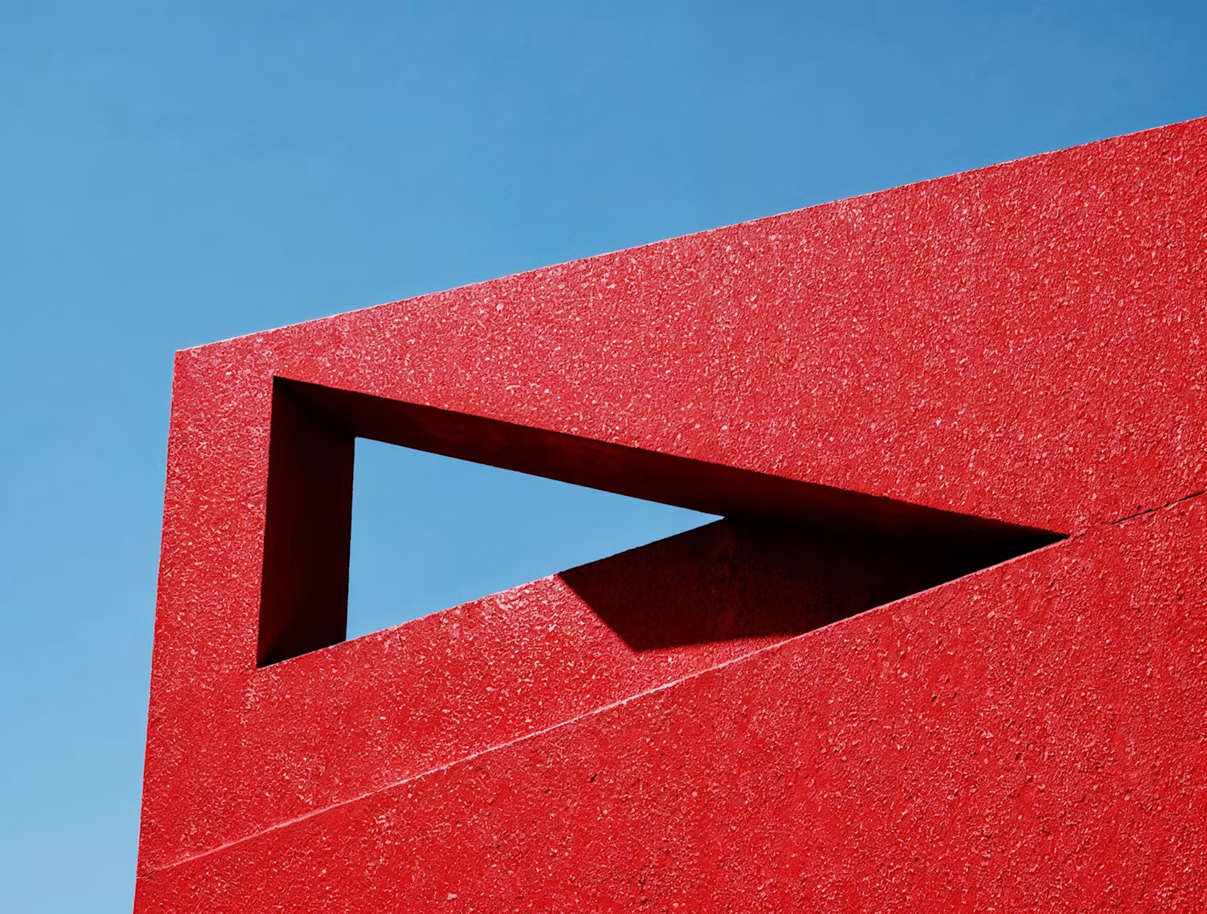 Red wall with a triangular cut-out against a blue sky