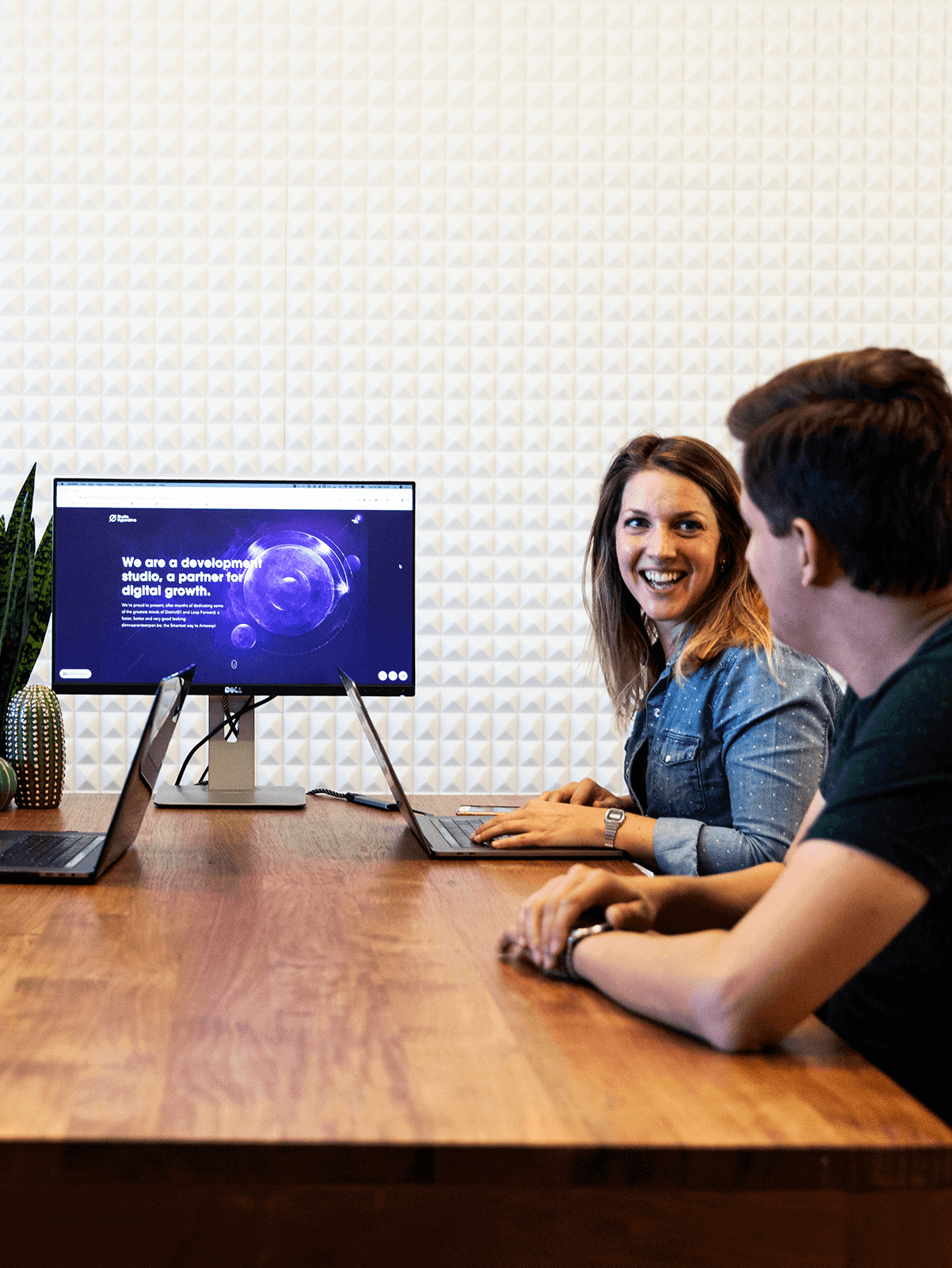Two people laughing while one of them gives a demo of a project on a computer scree