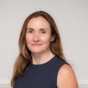 A woman with long brown hair and a faint smile, wearing a navy sleeveless top against a light background.