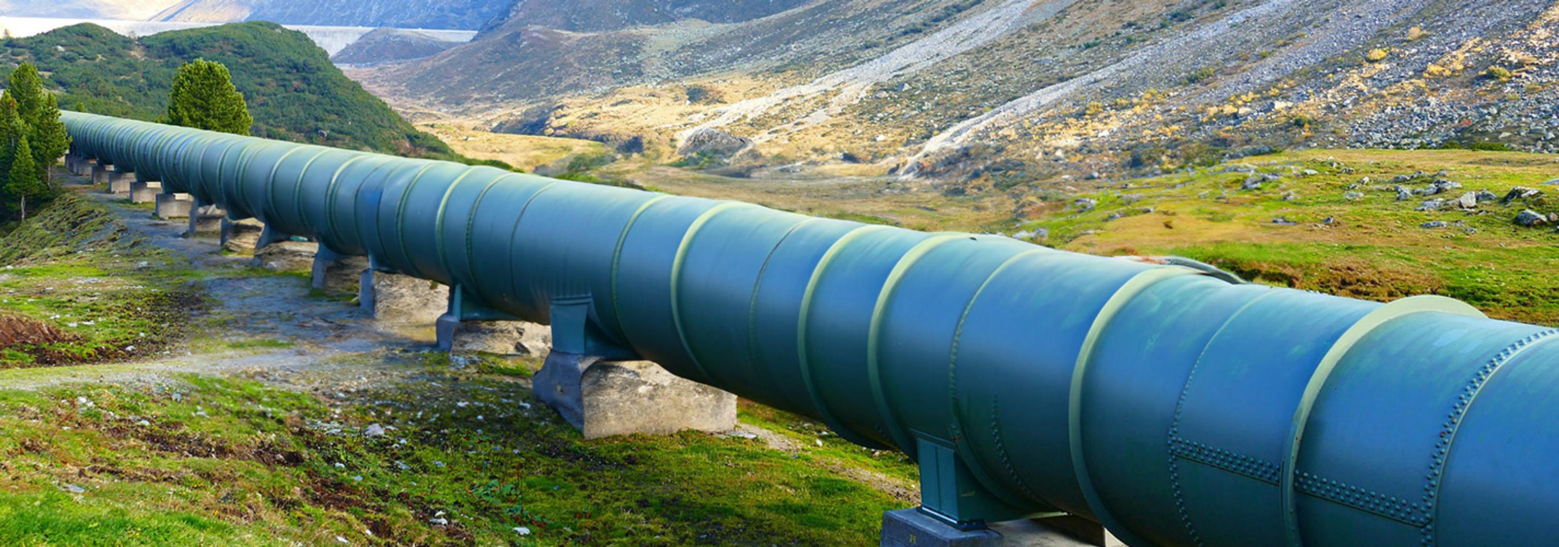 An elevated teal pipeline stretches across a grassy, mountainous landscape.