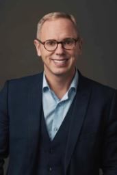 A smiling man wearing glasses and a blue suit.