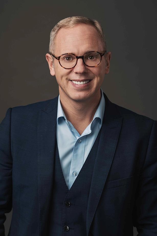 A smiling man wearing glasses and a blue suit.