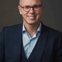 A smiling man wearing glasses and a blue suit.
