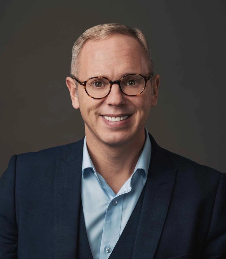 A smiling man wearing glasses and a blue suit.