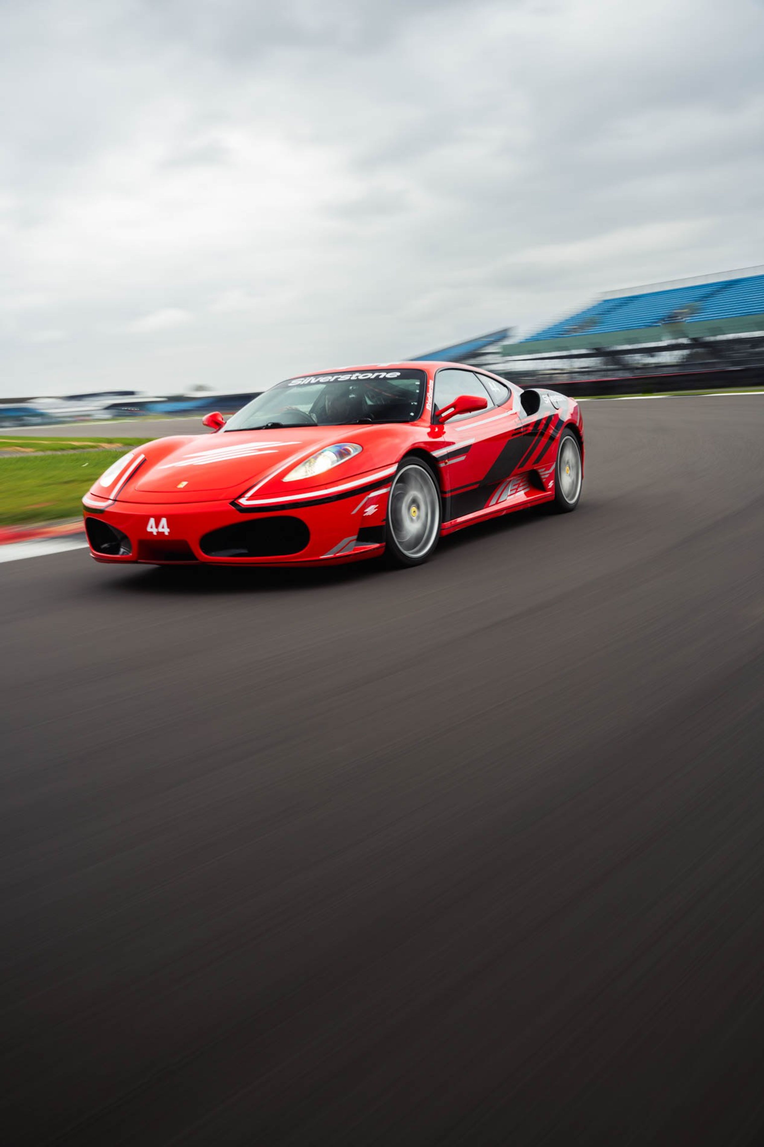 A red Ferrari sports car with black stripes and the number 44 races on a track, with 'Silverstone' on its windshield.
