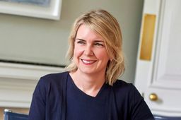 Smiling blonde woman wearing a navy top, looking left.