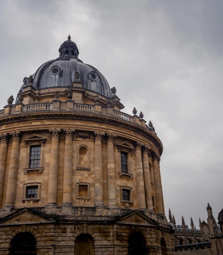 The Radcliffe Camera, a grand circular stone building with a large dome, under a cloudy sky.
