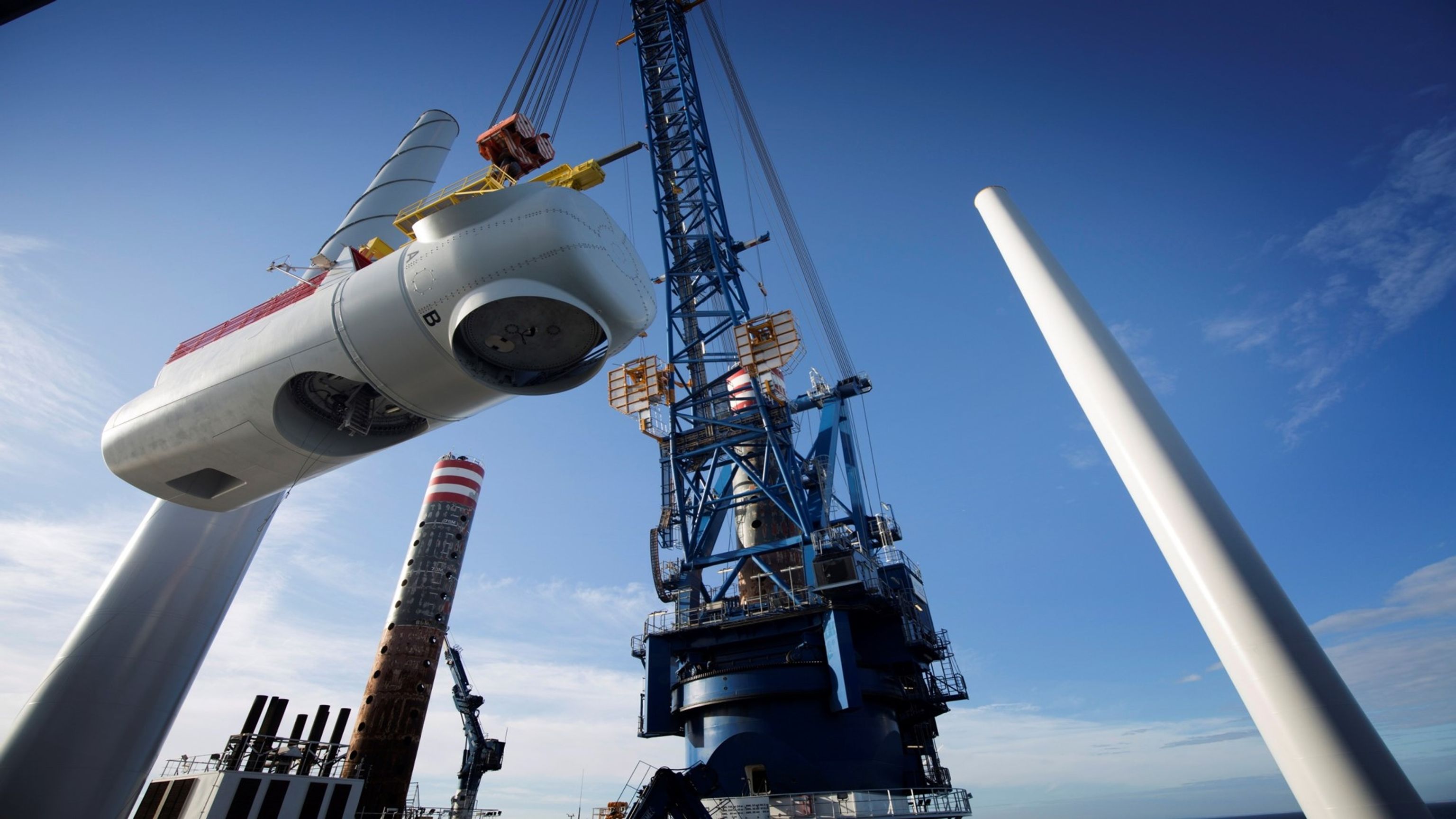 a large crane is lifting a wind turbine on top of a boat .