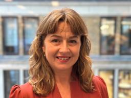 Professional headshot of Sophie White, a woman facing the camera with a neutral background, dressed in smart casual attire and smiling softly.