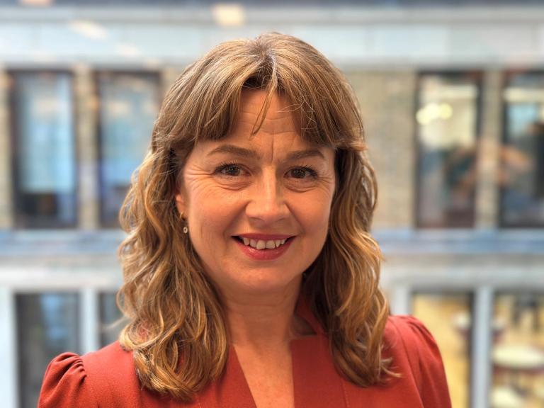 Professional headshot of Sophie White, a woman facing the camera with a neutral background, dressed in smart casual attire and smiling softly.